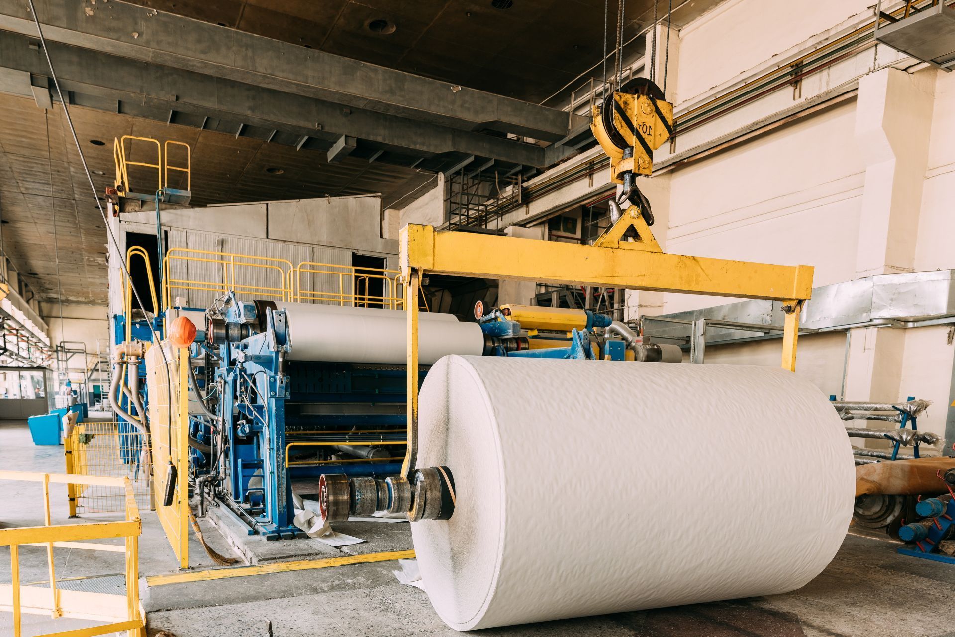 Industrial paper mill with a large white paper roll being handled by yellow machinery