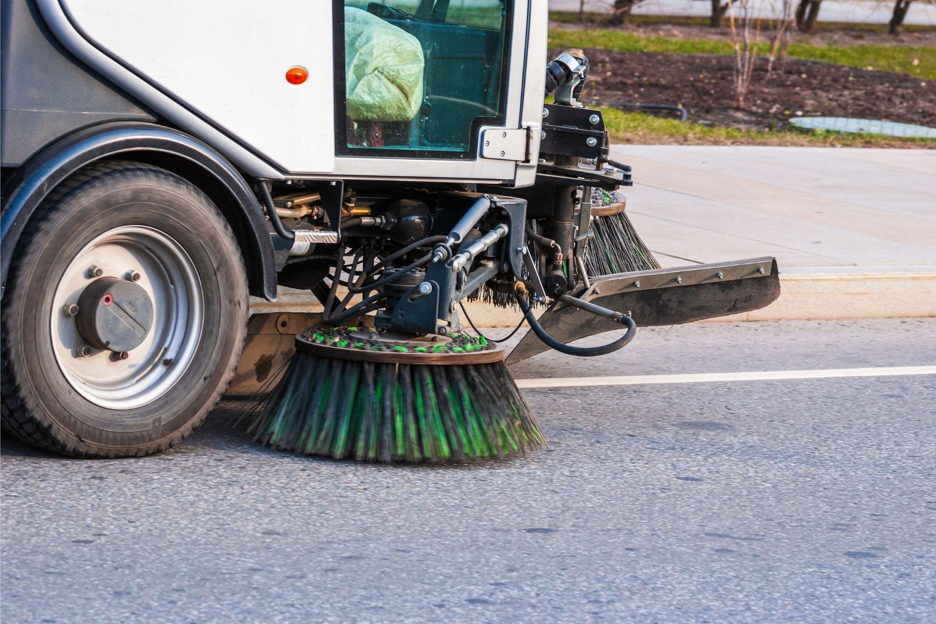 Street sweeper truck cleaning a road, with green rotating brushes on the pavement