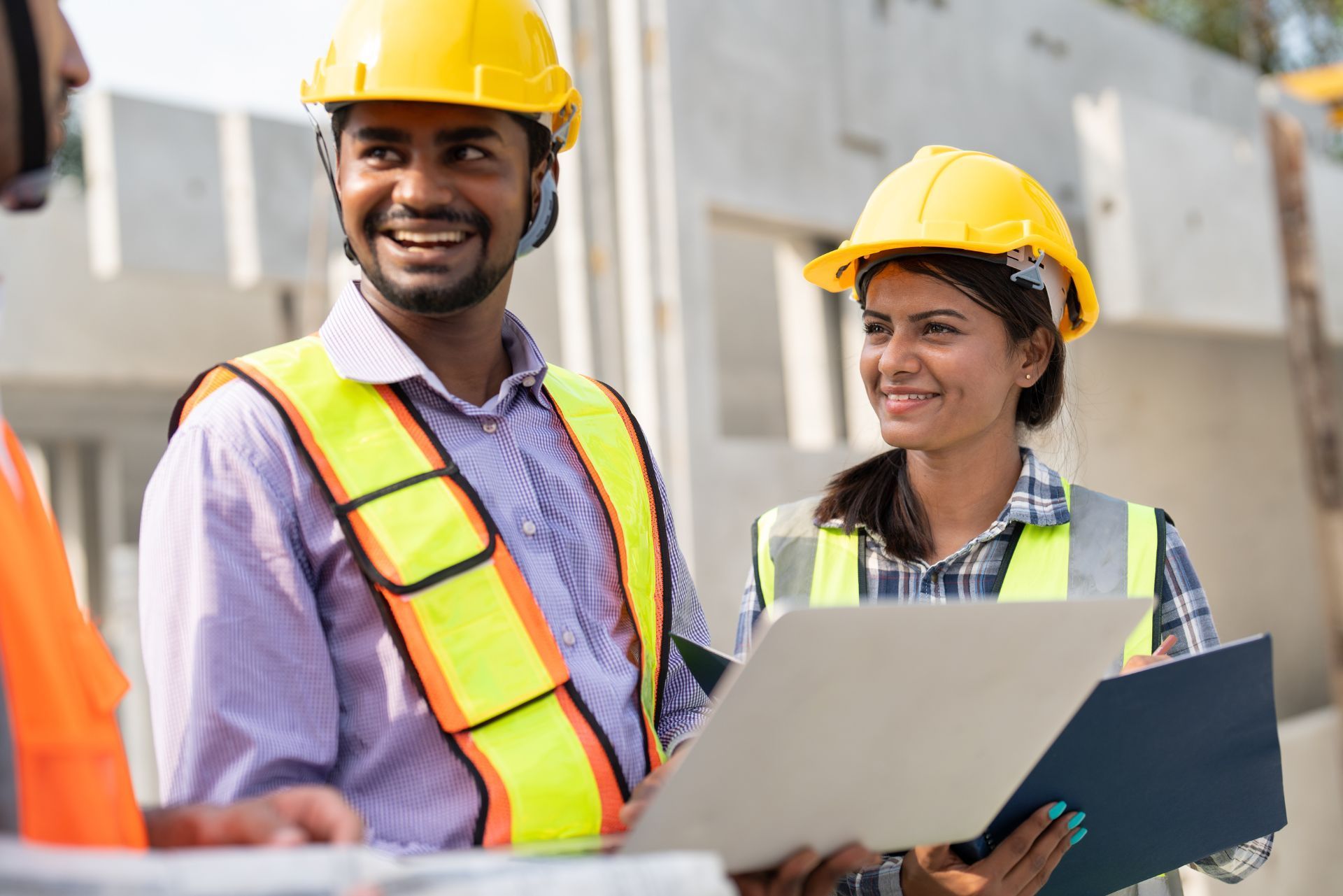 Two construction workers in hard hats reviewing plans outdoors
