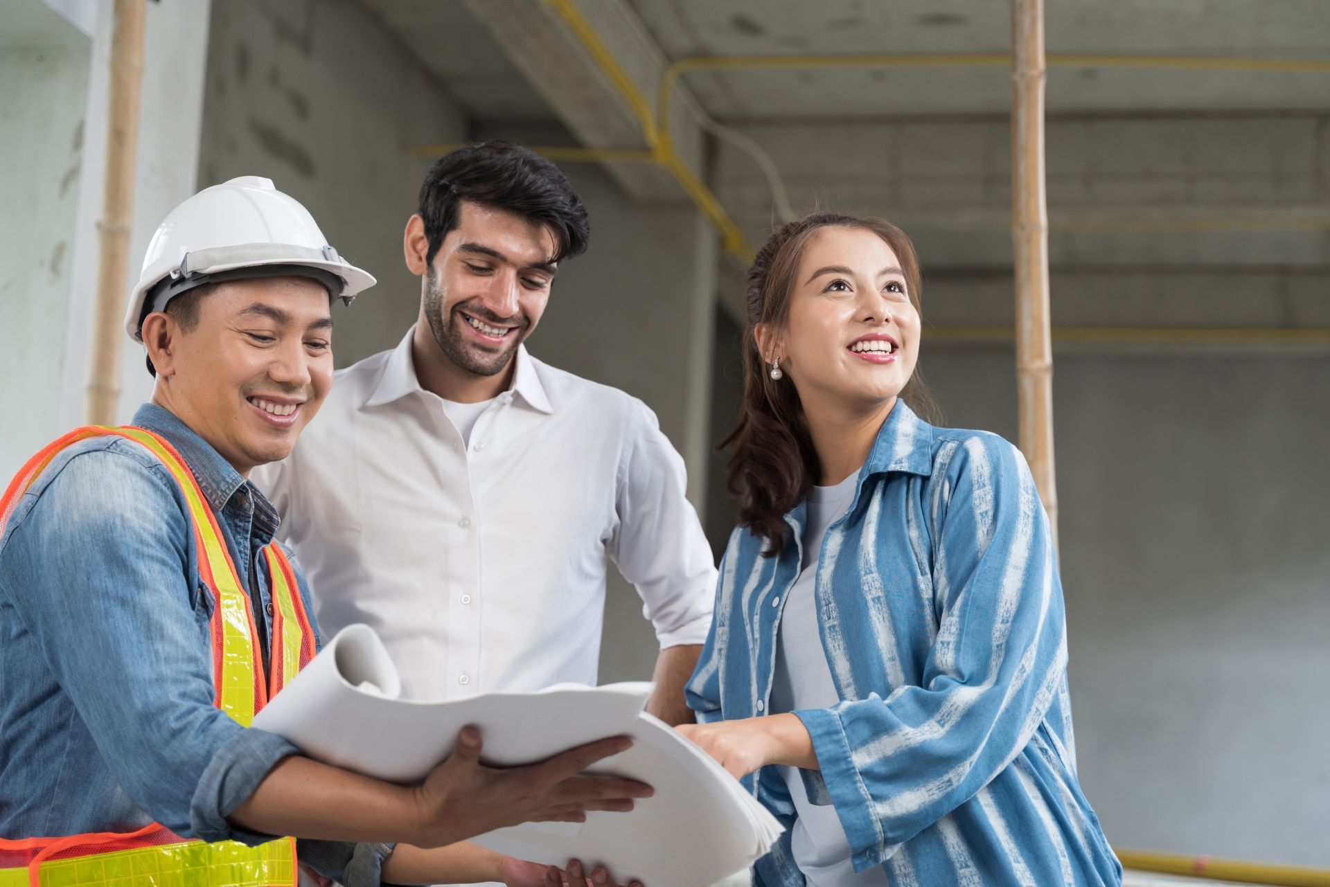 Three construction workers reviewing blueprints on a building site, smiling and talking together.