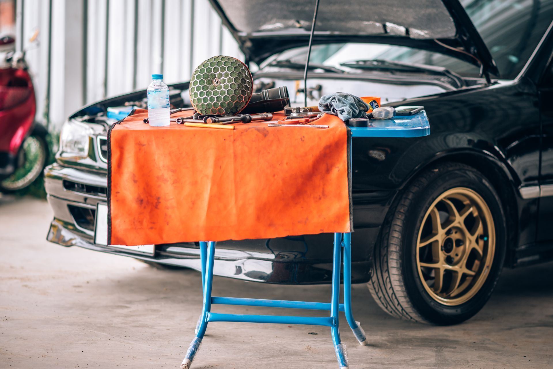 Car on jack with hood open beside a small table covered in an orange cloth and tools