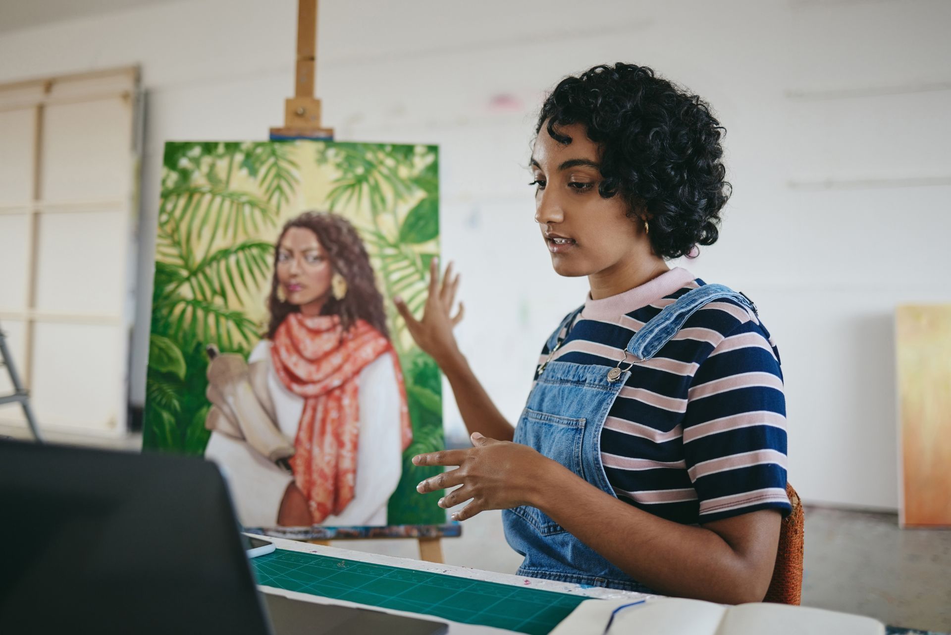 Artist painting a portrait in a studio, with a reference painting on an easel behind them.