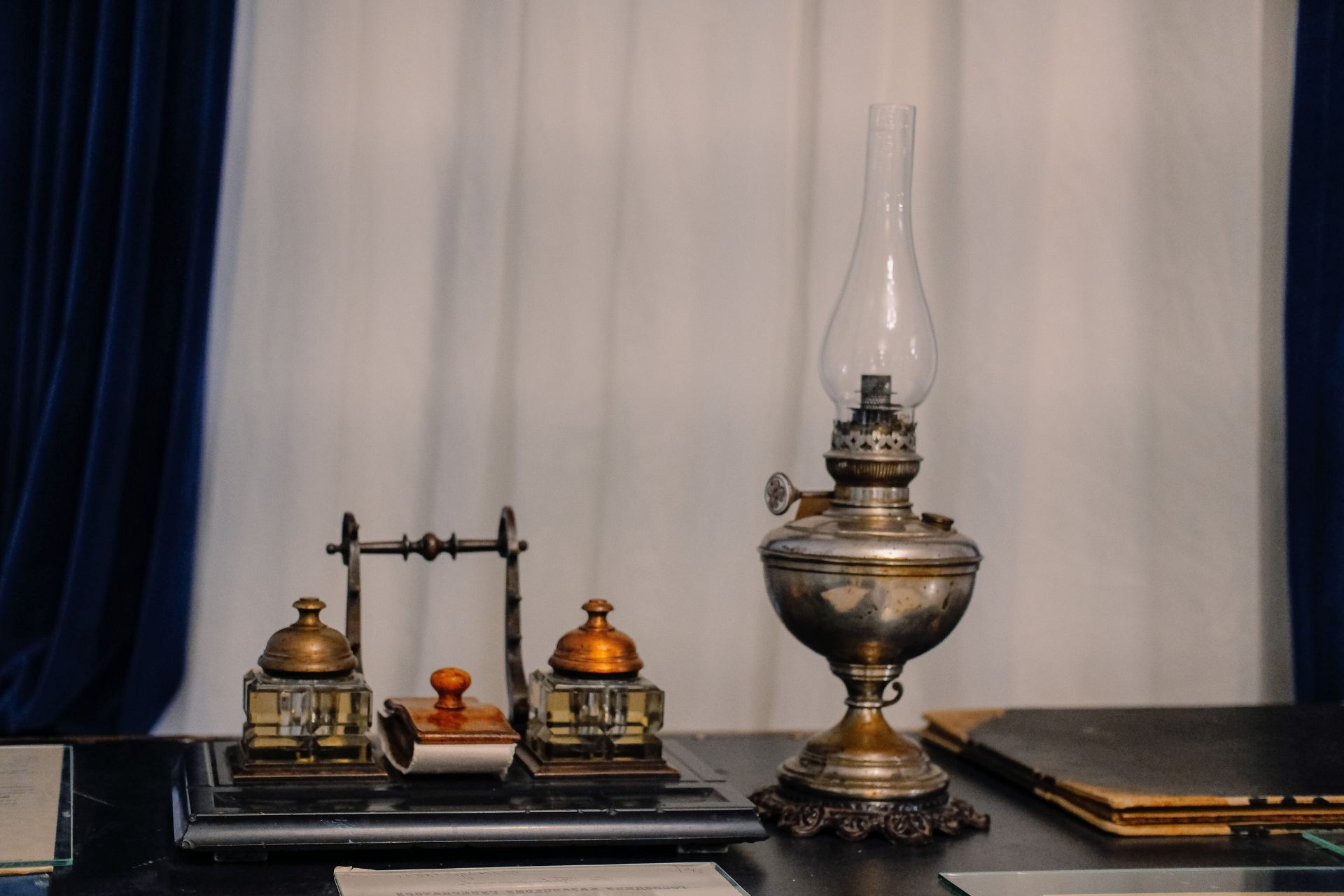 Antique lamps and decorative items on a table against white and dark blue curtains
