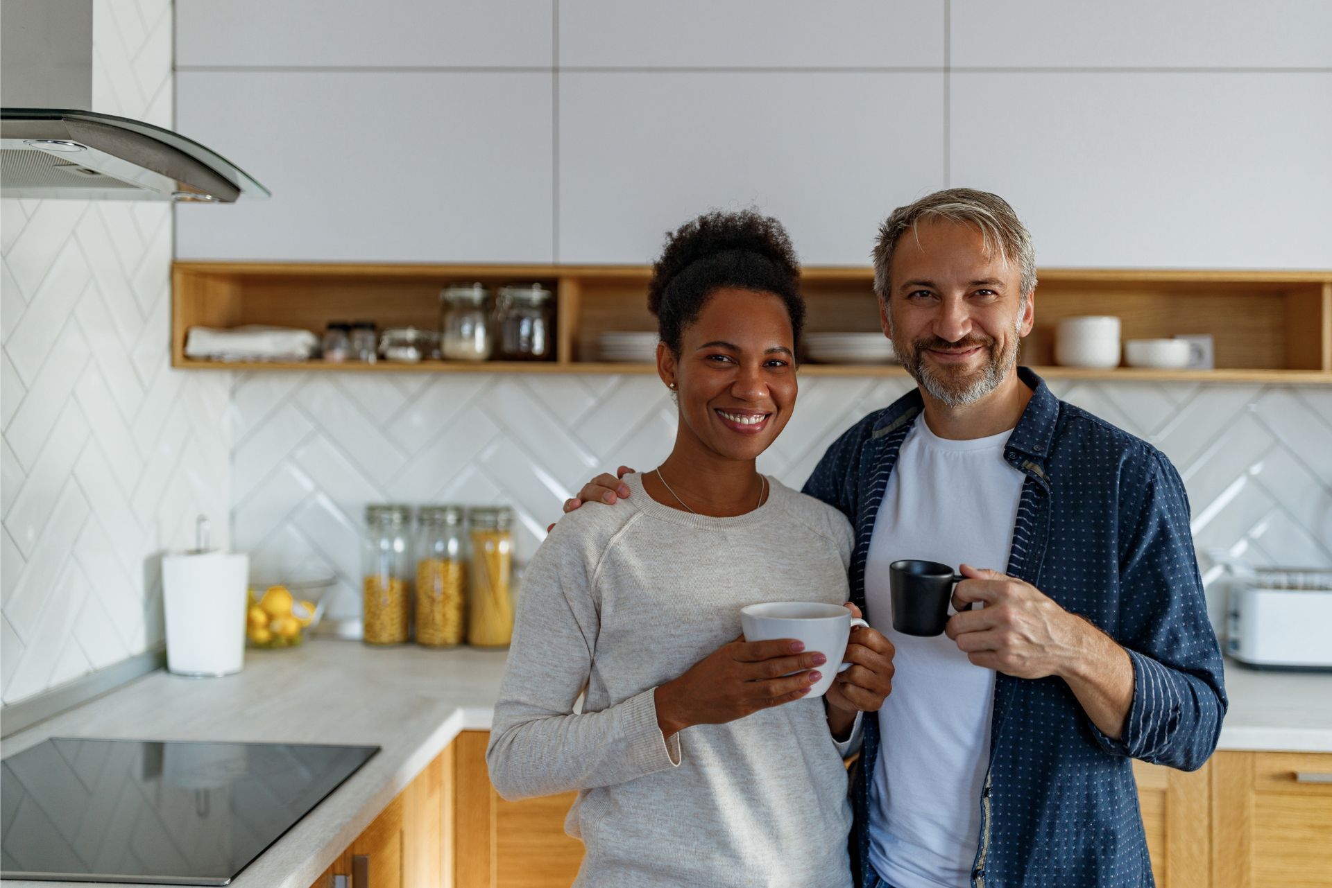 Two people smiling and holding mugs in a bright modern kitchen