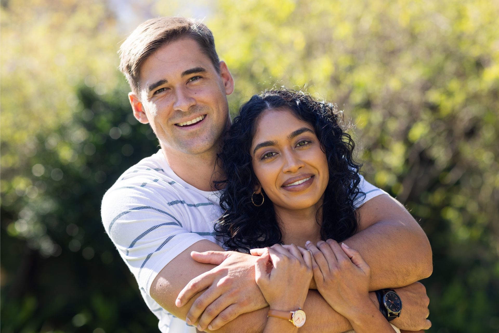 Two people smiling and hugging outdoors in a sunlit garden