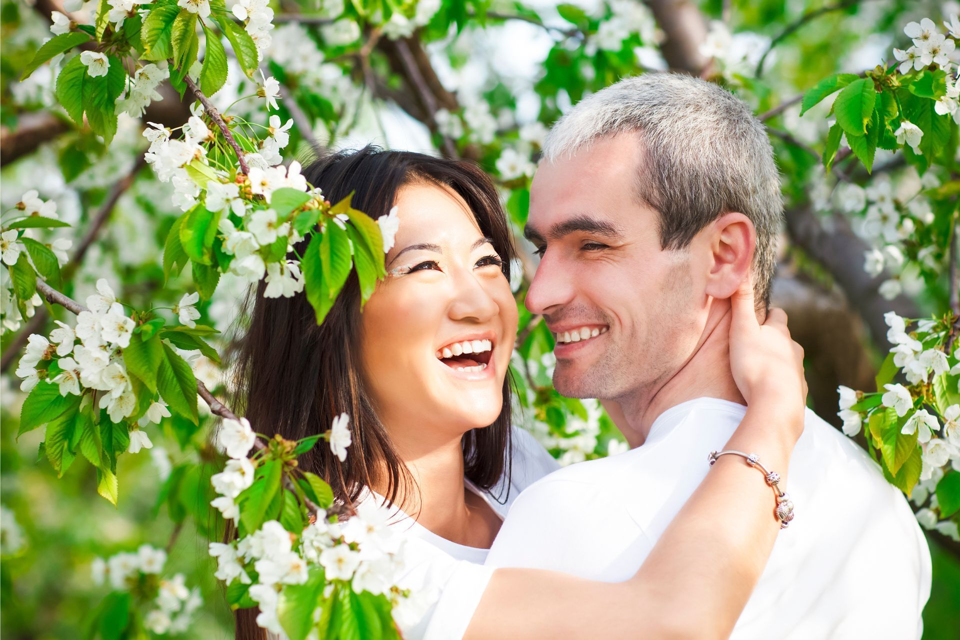 Smiling couple embracing among green leaves outdoors