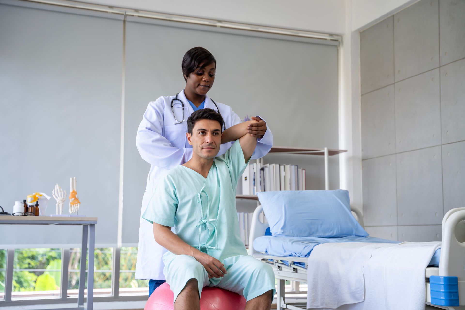 Healthcare worker applying treatment to a seated patient in a clinic room with a medical bed.