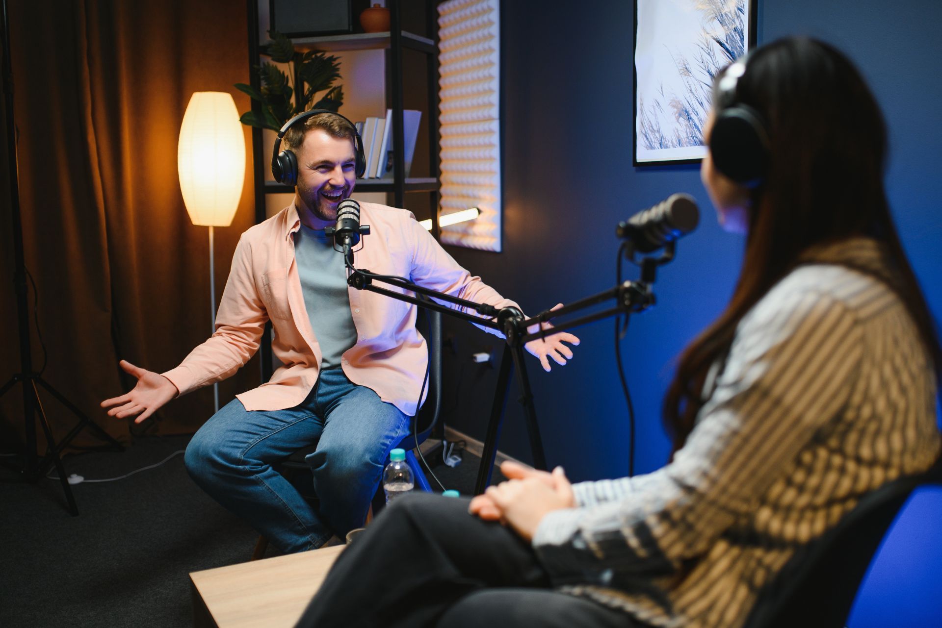 A person in a peach shirt gestures while speaking into a microphone during a podcast interview in a studio.