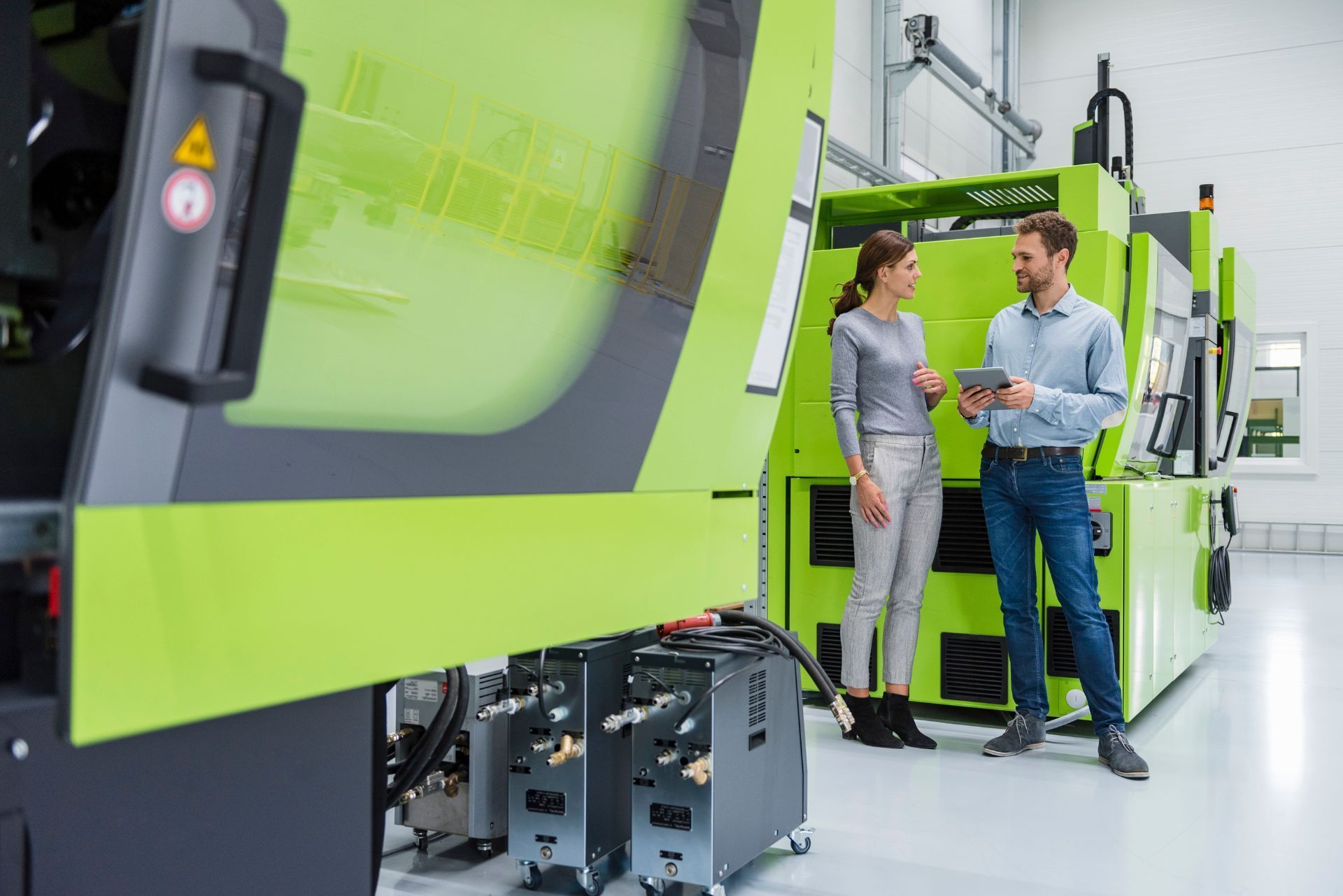 Two people discussing beside a large green industrial machine in a factory
