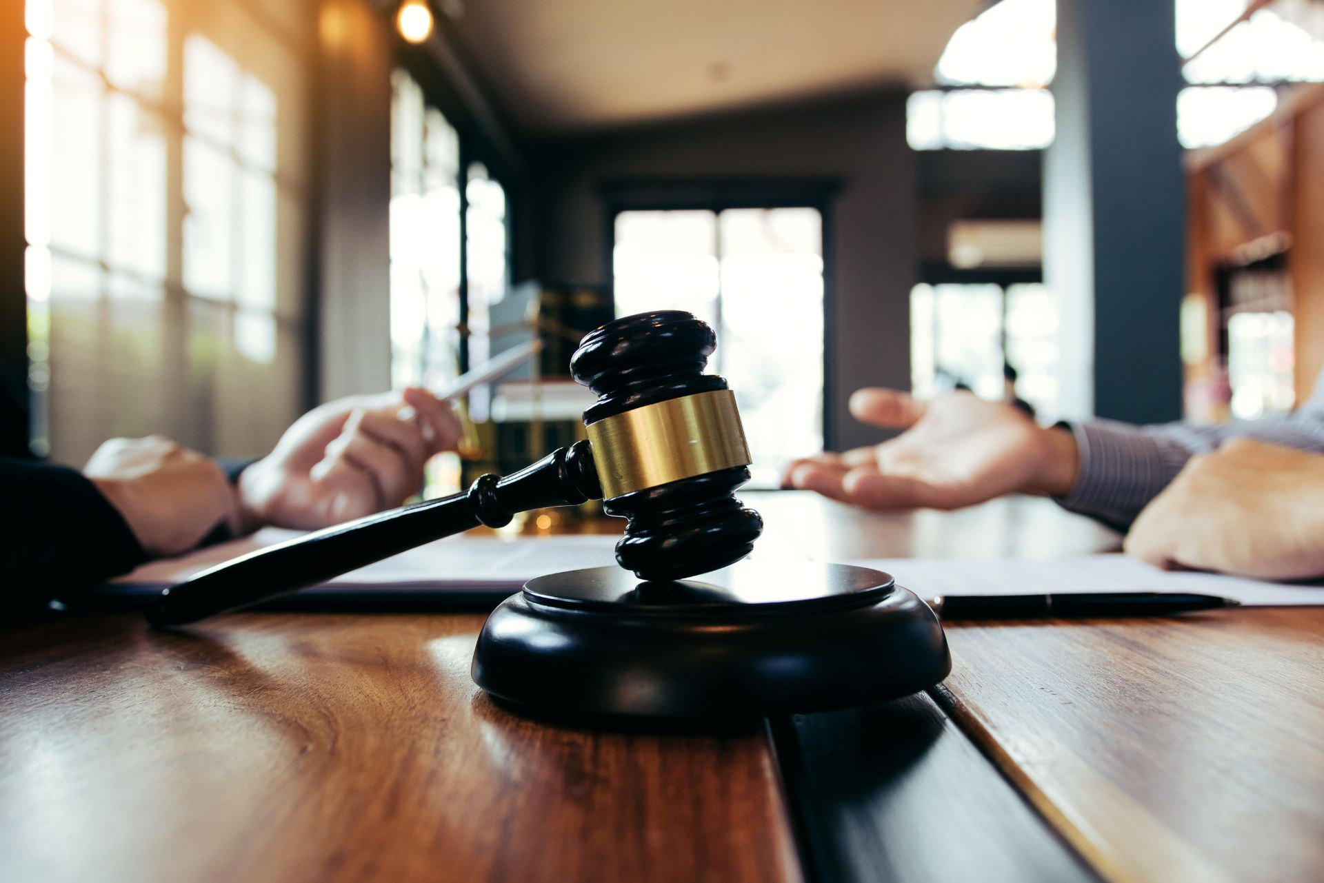 Judge's gavel on a wooden table in a courtroom, with two people seated across from each other.