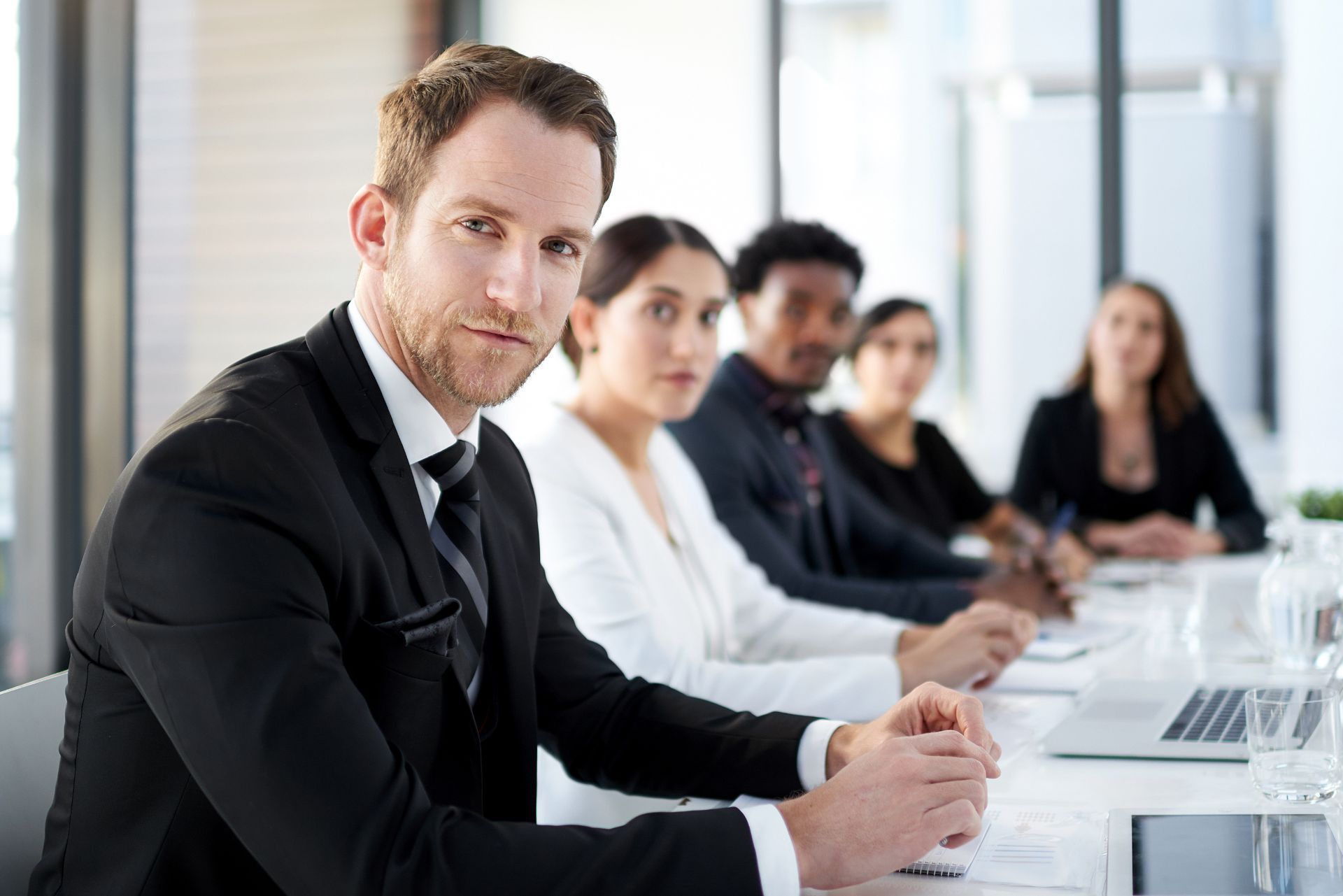 Business meeting in a bright conference room with people seated at a table and laptops open