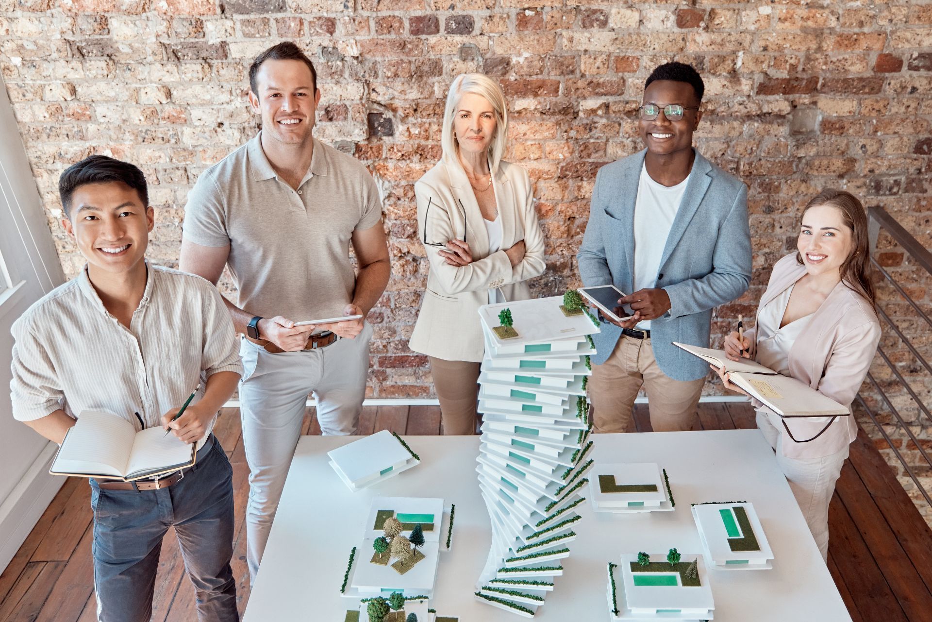 Team gathered around a table with a tall stack of cards, smiling in a brick-walled office