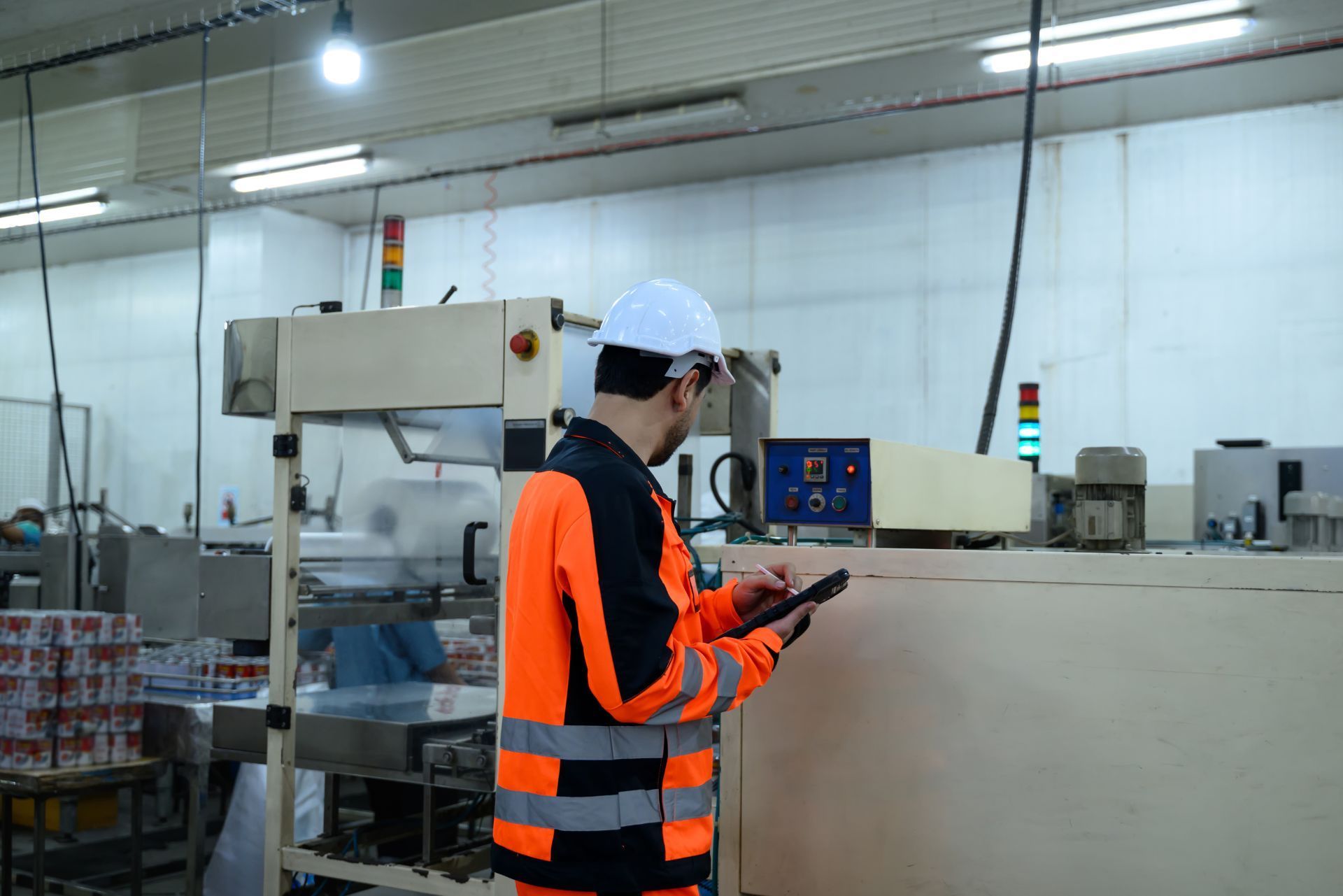 Worker in orange safety vest inspecting machinery on a factory floor
