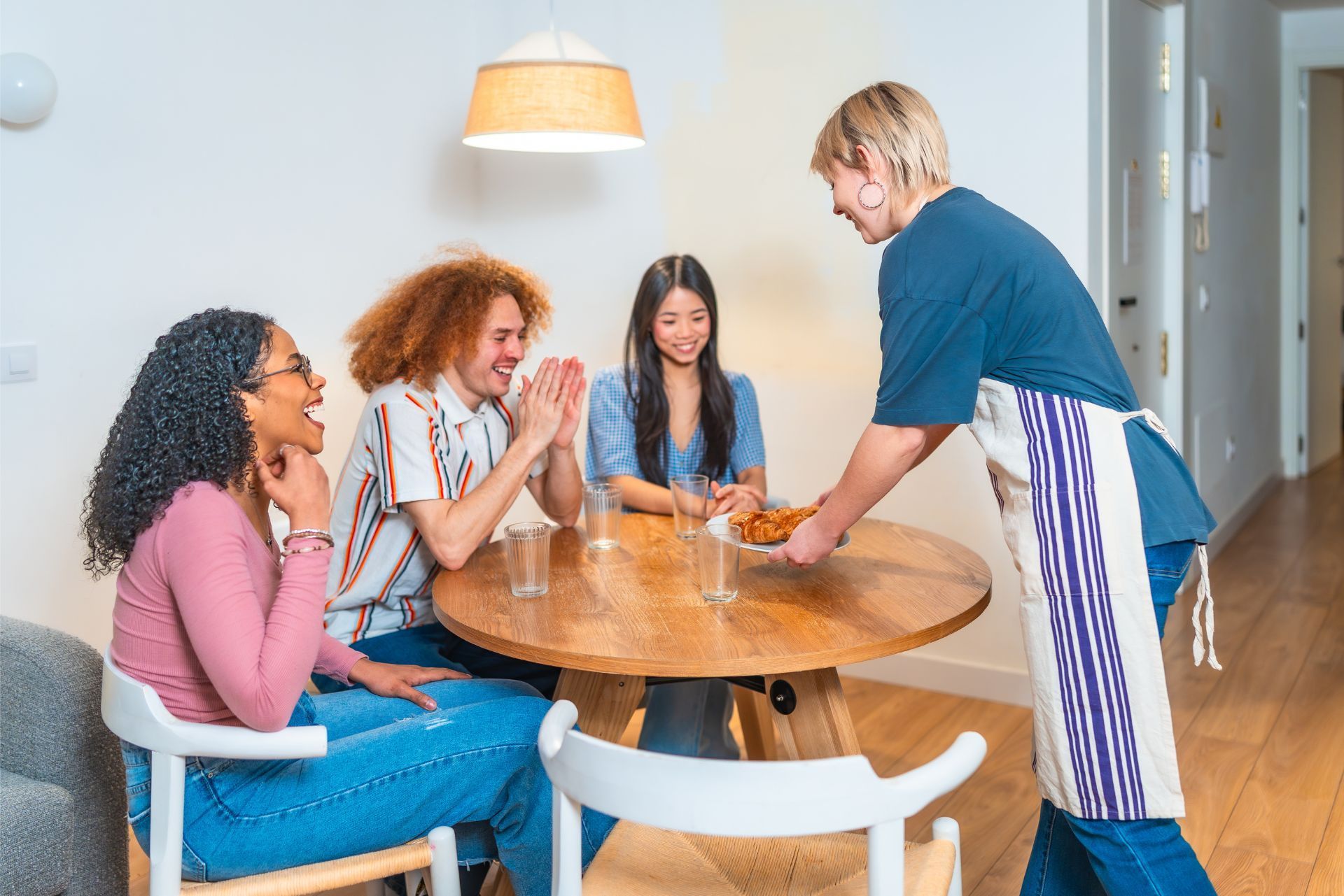 Four people chatting around a round wooden dining table in a bright kitchen