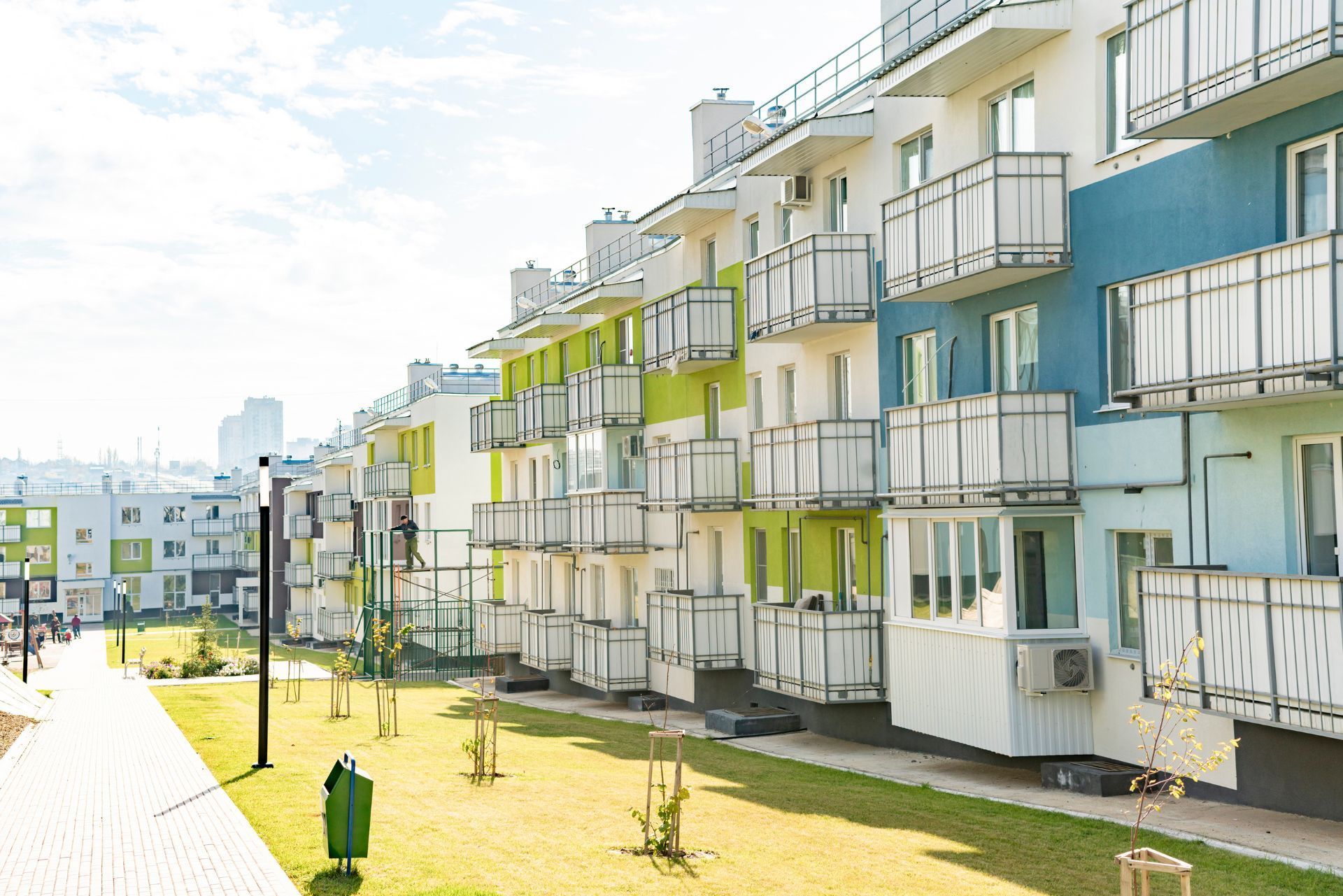 Modern apartment buildings with balconies along a sunny walkway and grassy area