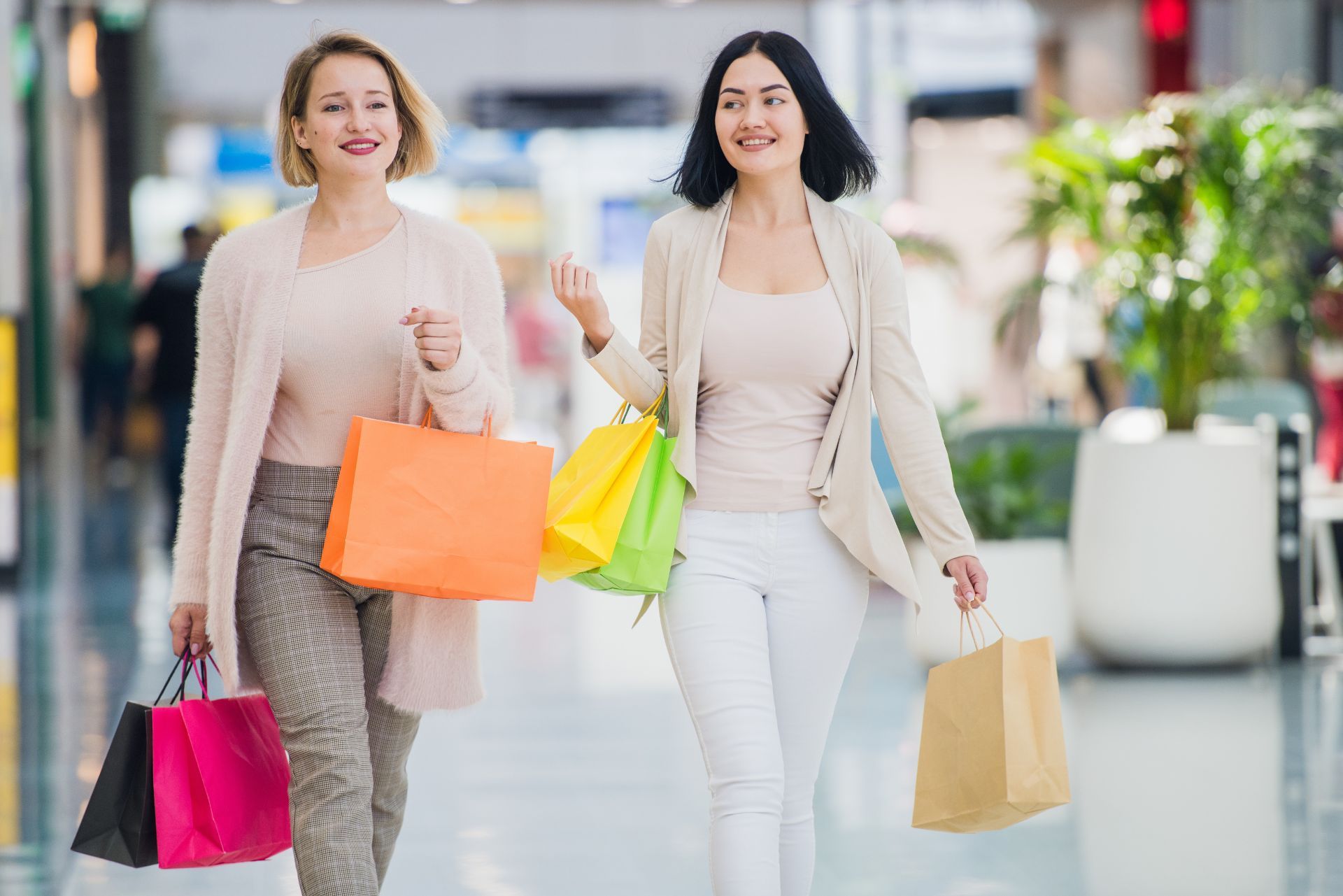 Two women shopping outdoors, smiling and carrying colorful shopping bags