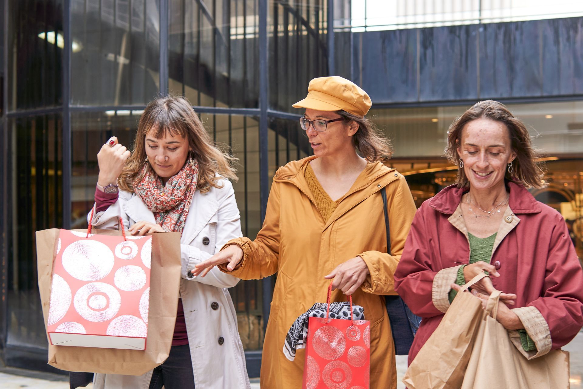 Three people walking outdoors with shopping bags, smiling in front of a building.