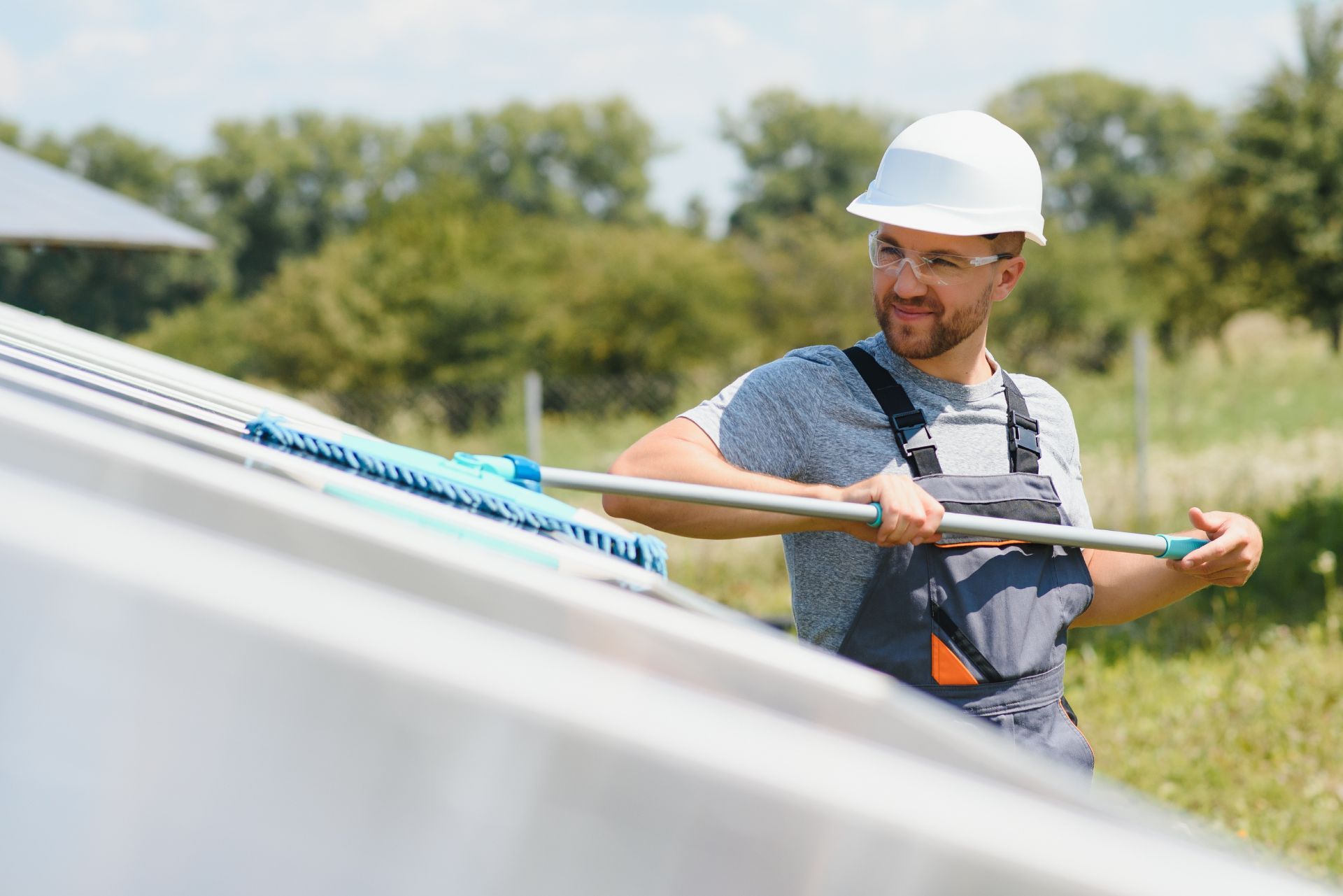 Worker in hard hat cleaning solar panels outdoors with a long brush