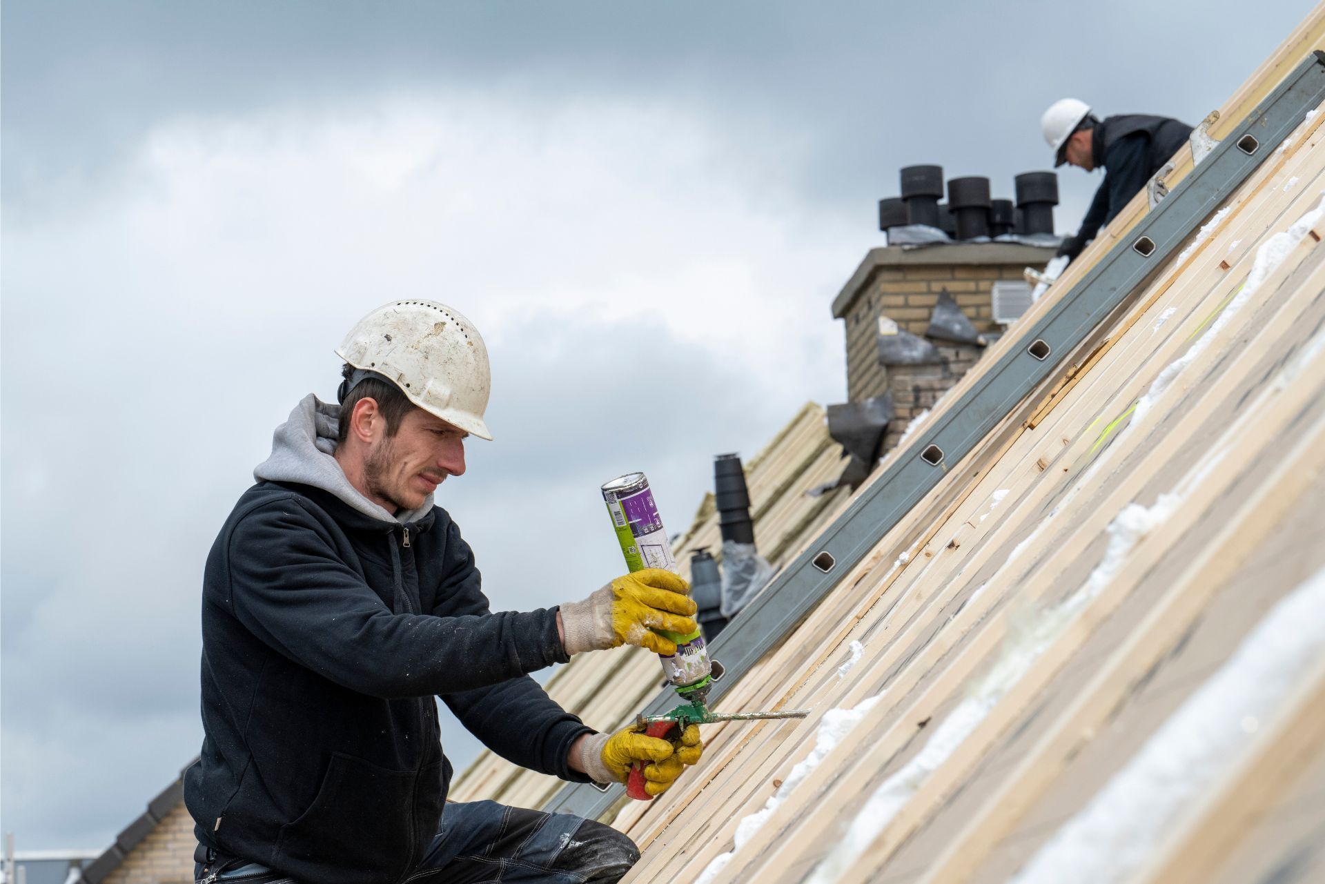 Workers installing roof shingles on a sloped roof with tools and safety gear
