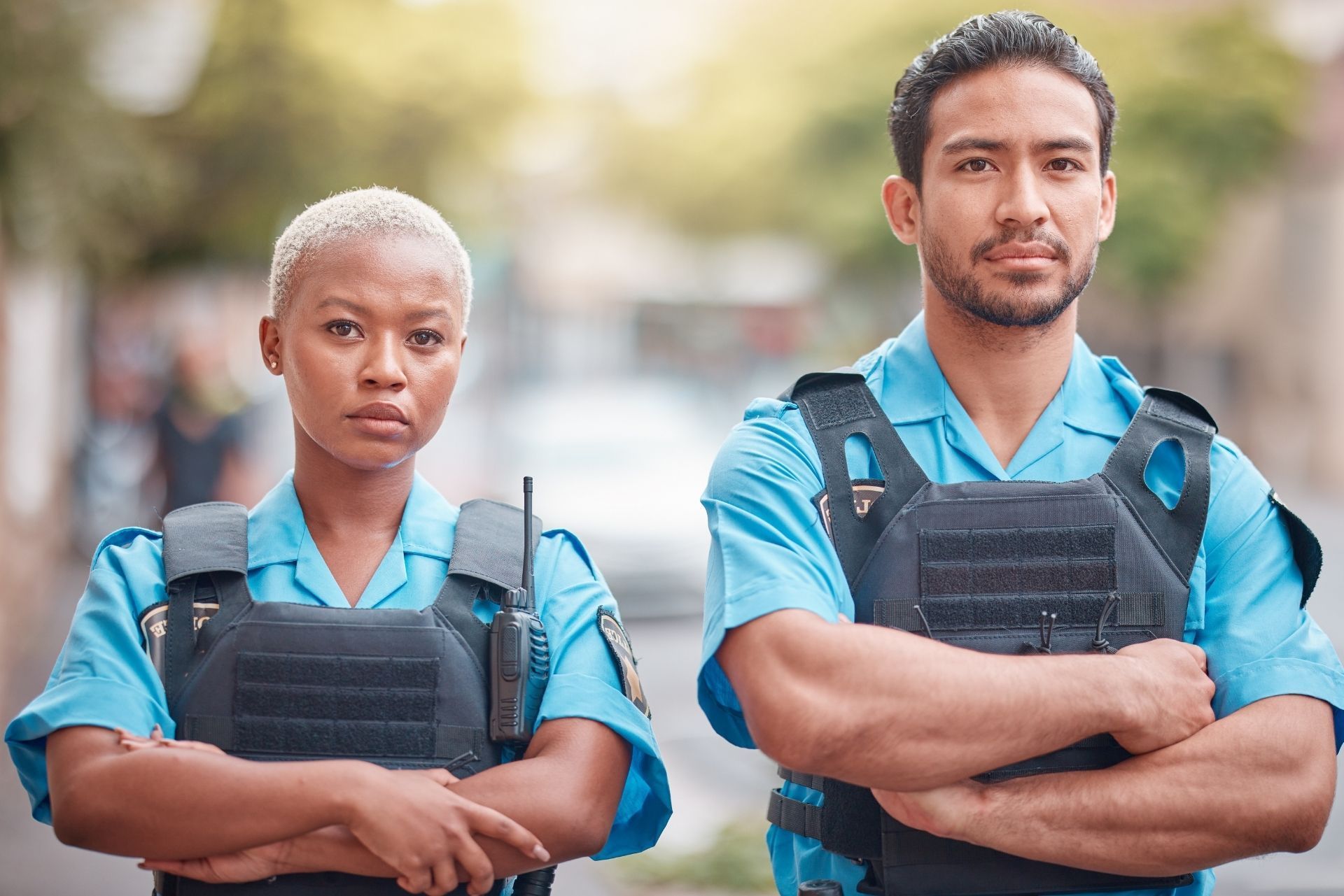Two security officers in blue uniforms and black vests standing with arms crossed outdoors