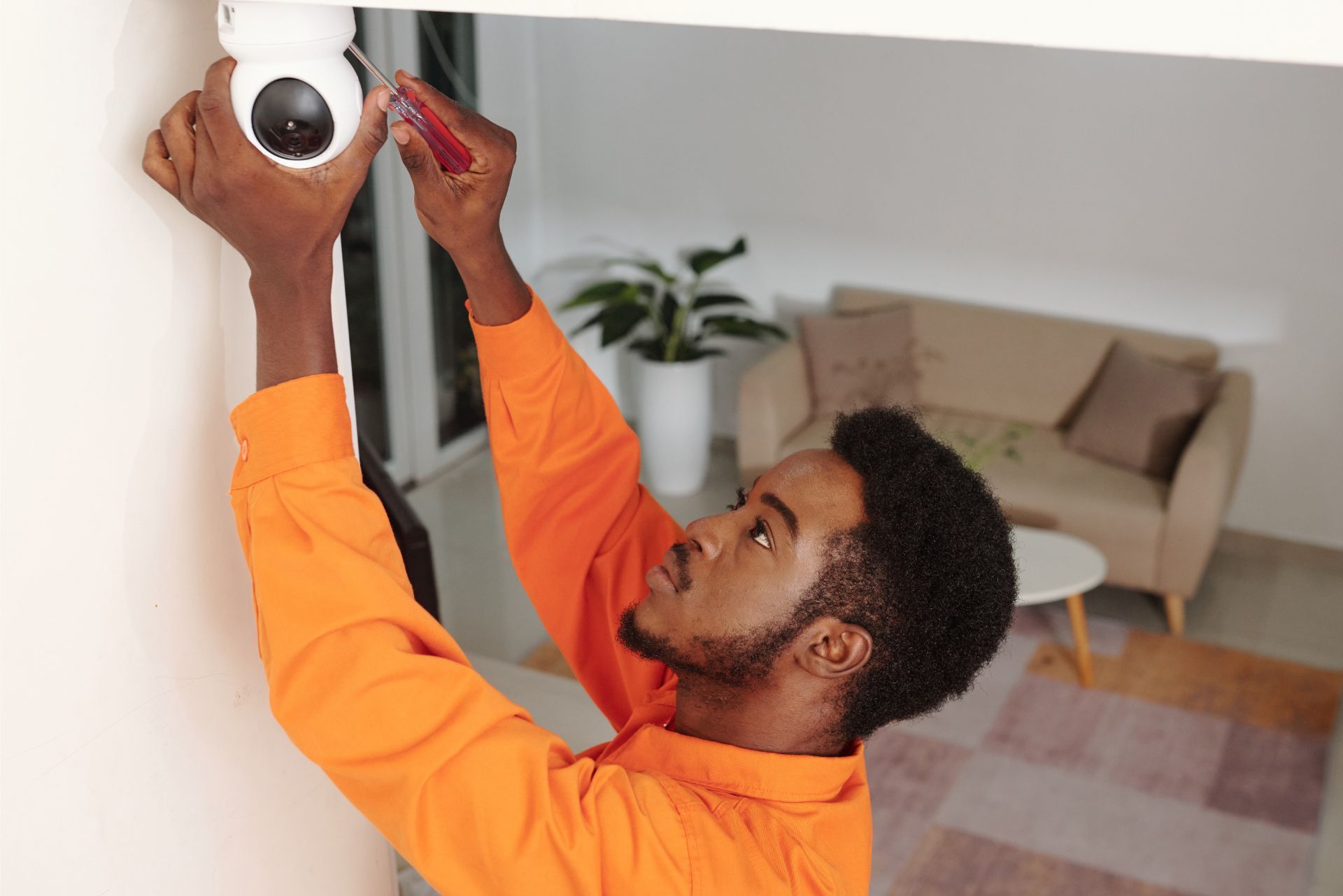 Technician installing a white security camera on a wall in a living room