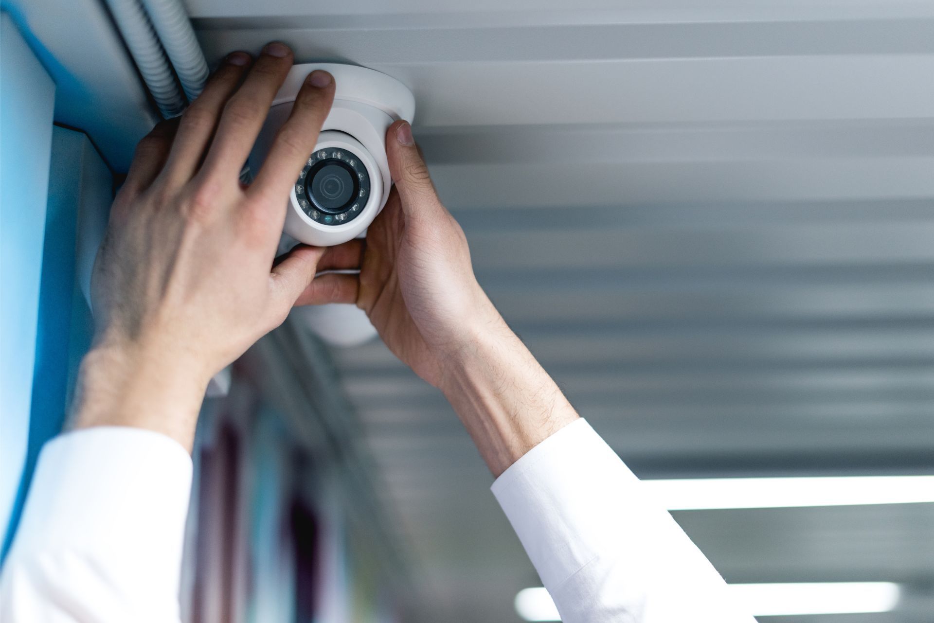 Hands installing a white security camera near a ceiling indoors