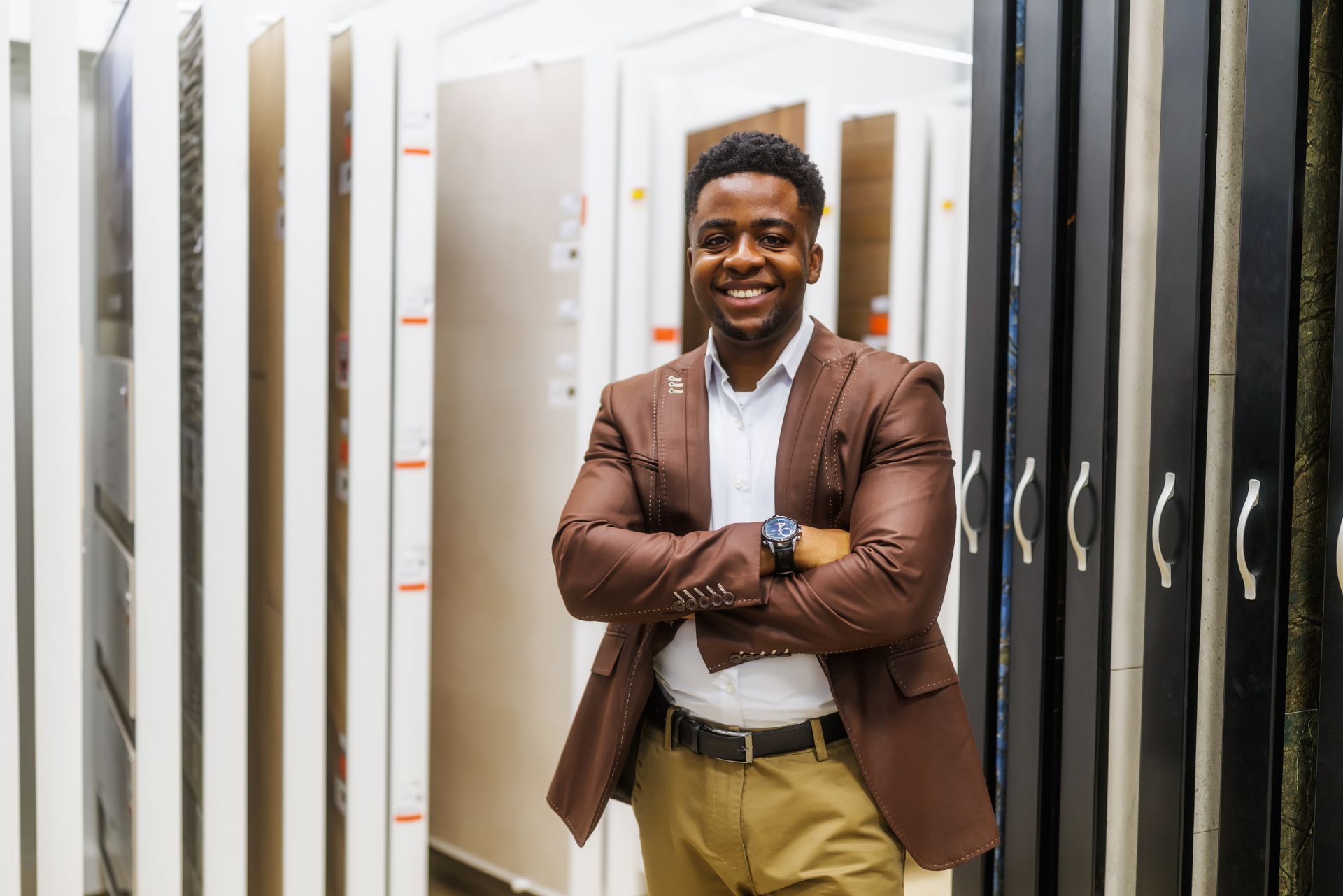 Smiling man in brown blazer stands with arms crossed in a lighting showroom