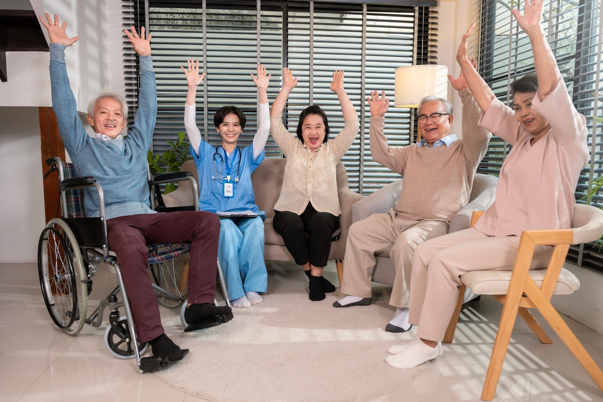 Five people in a bright room raising their arms in a group exercise or celebration, one in a wheelchair