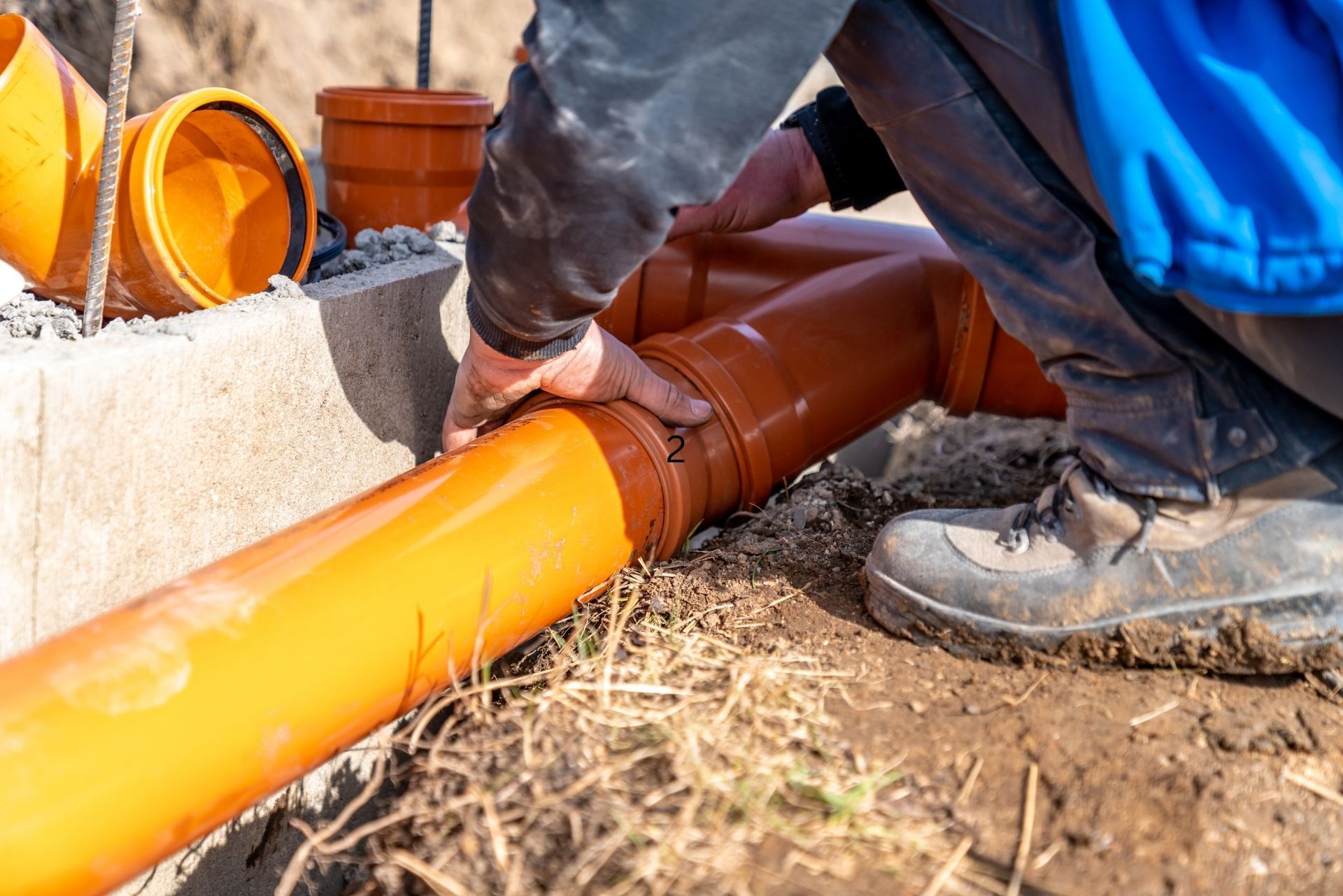A worker connects orange PVC drainage pipes at a construction site.