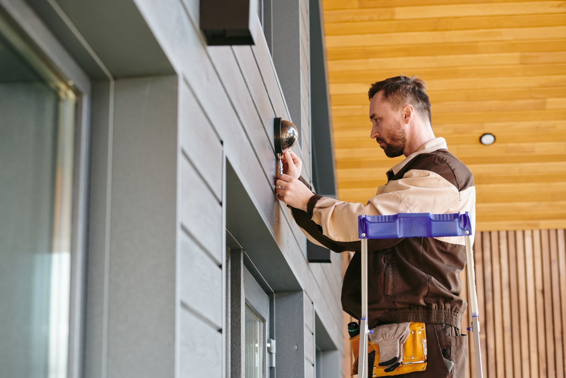 Man using a drill to install a fixture on an exterior wall beside a wooden fence