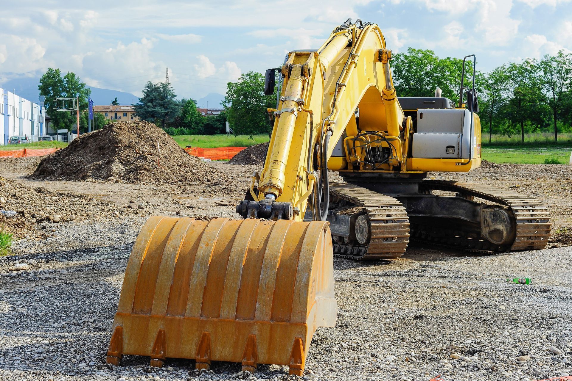 Yellow excavator on a gravel construction site with dirt piles and trees in the background