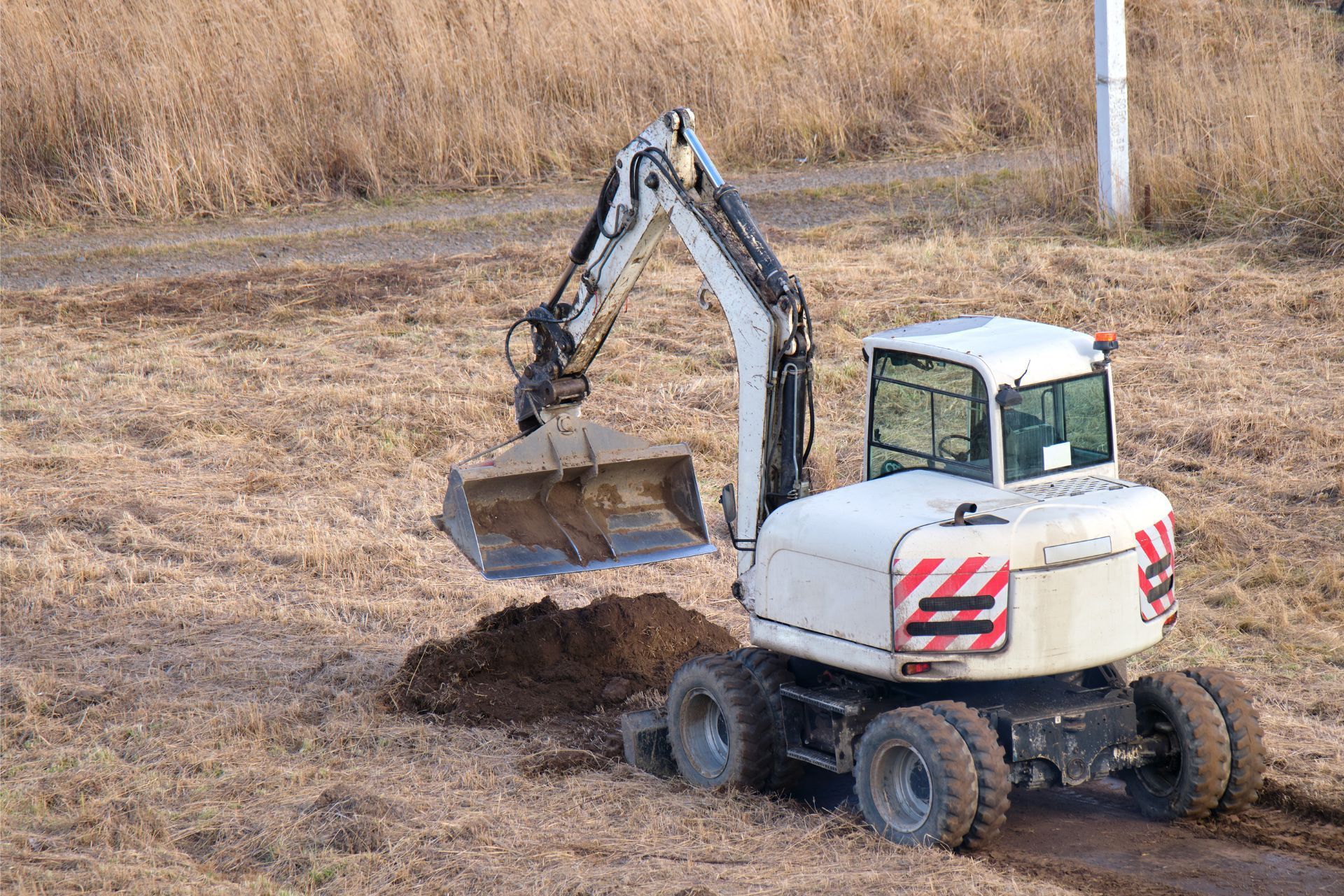 White excavator with raised bucket on dry dirt field
