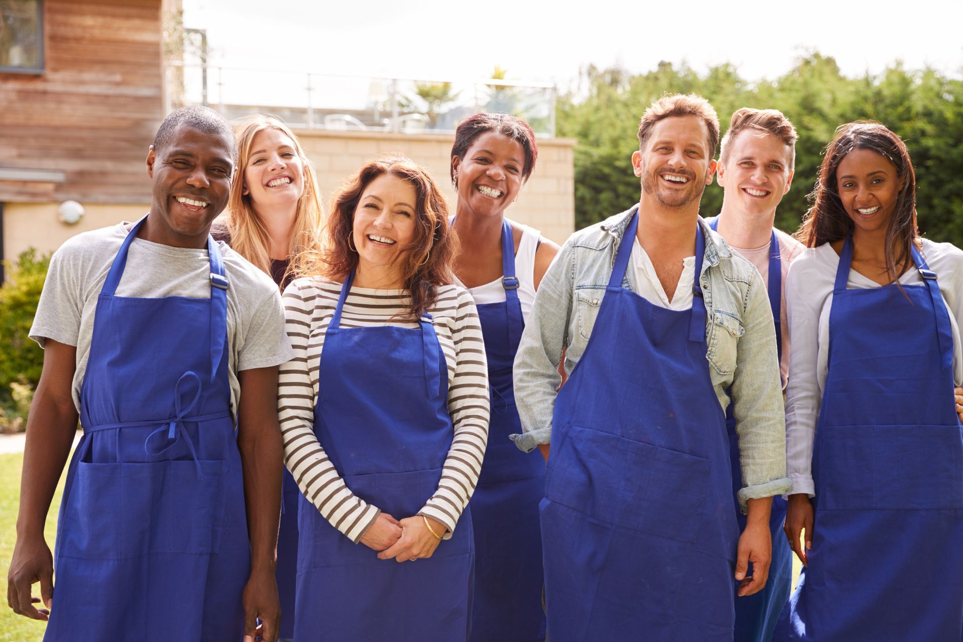 Group of smiling people in blue aprons standing outdoors in a garden