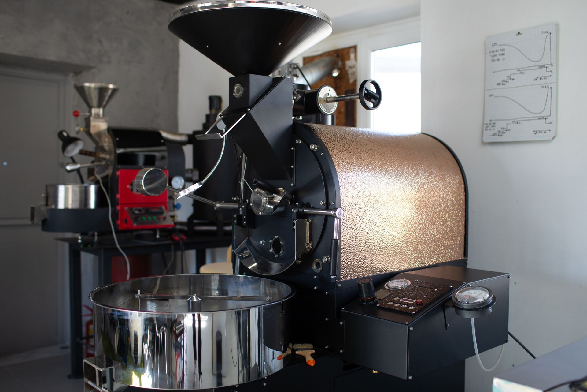 Coffee roaster machine in a workshop, with a metal drum and hopper, shown from the side.