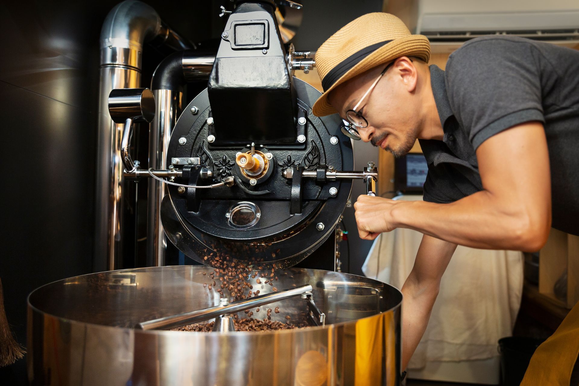 Person inspecting coffee beans pouring from a roasting machine into a metal bin