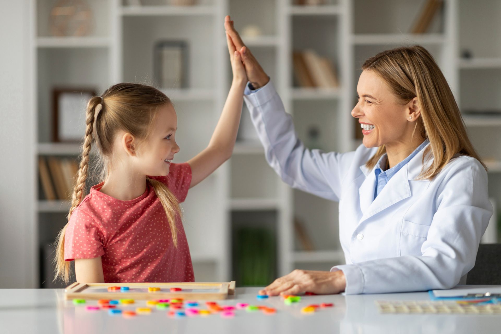 Child and adult high-five at a table with colorful pieces in a classroom