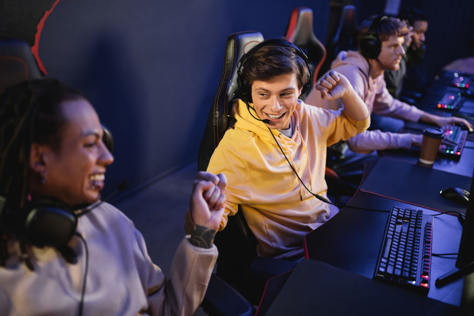 Gamers cheering at a computer gaming station, smiling and raising fists under colorful lights