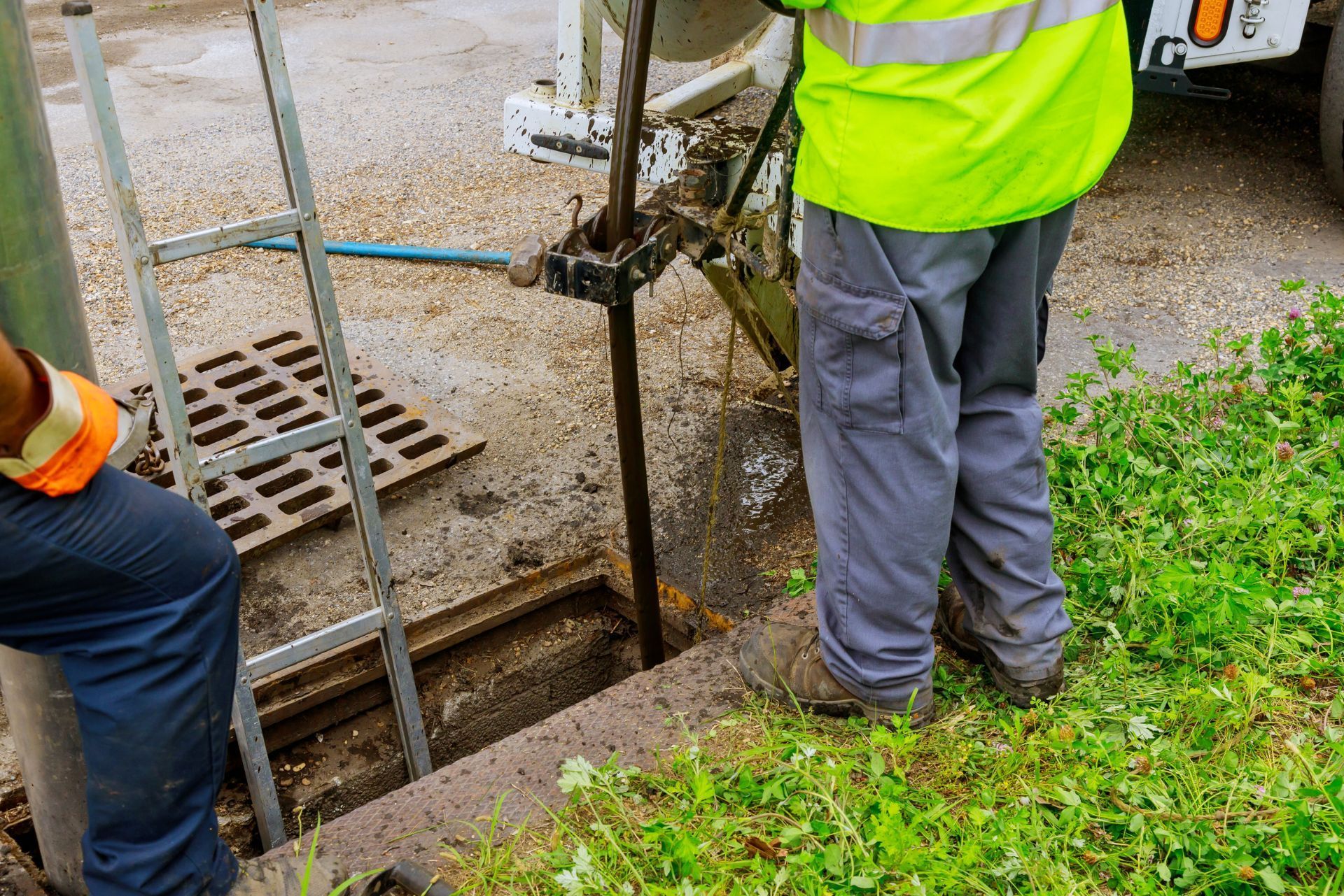 Workers in high-visibility gear inspecting a trench beside a sidewalk and storm drain