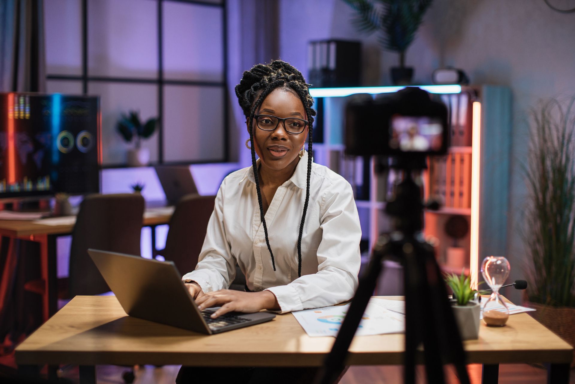 Person working on a laptop at a desk in a colorful home office, filming with a camera in the foreground
