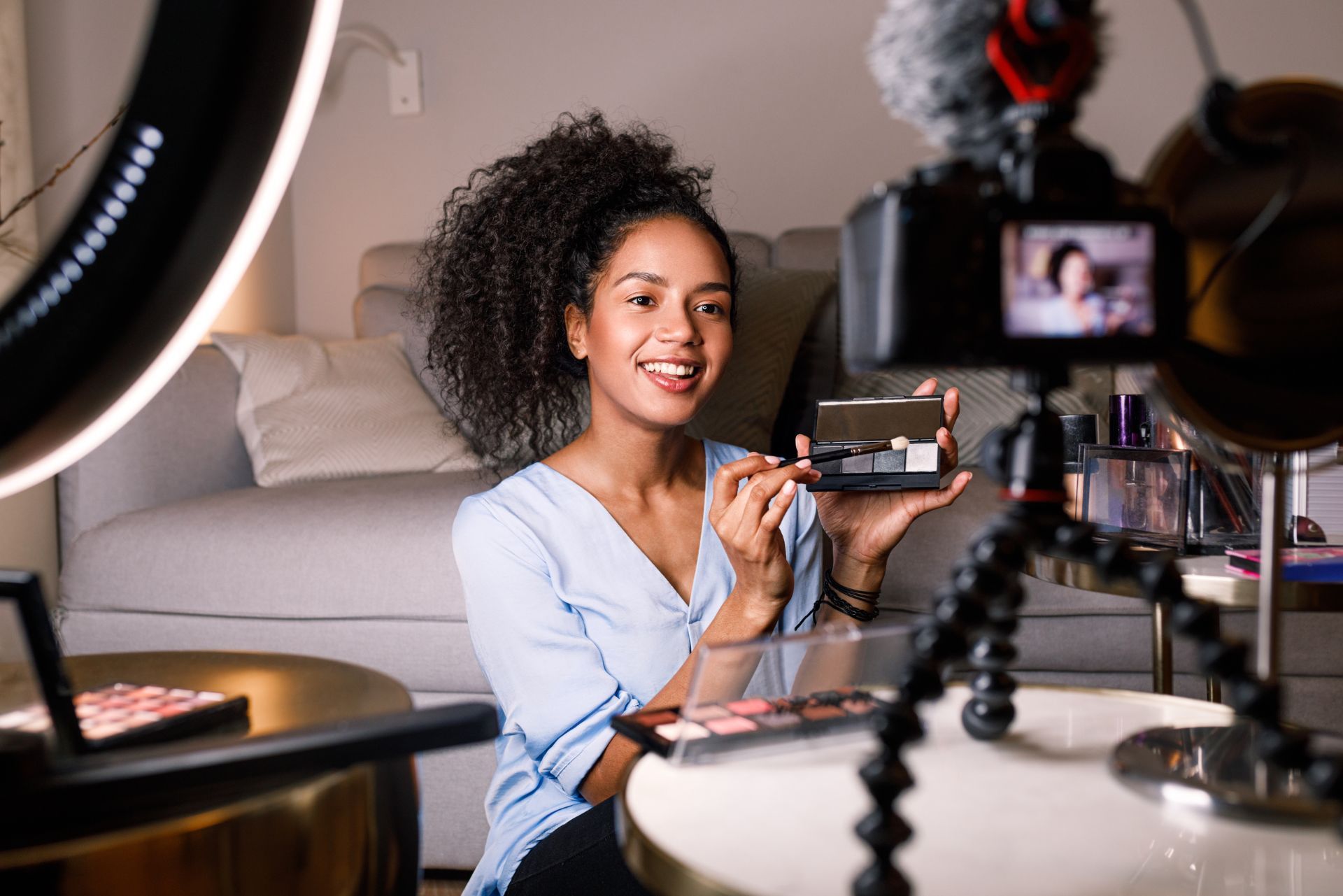 Woman filming a makeup tutorial at a vanity with a ring light and camera setup
