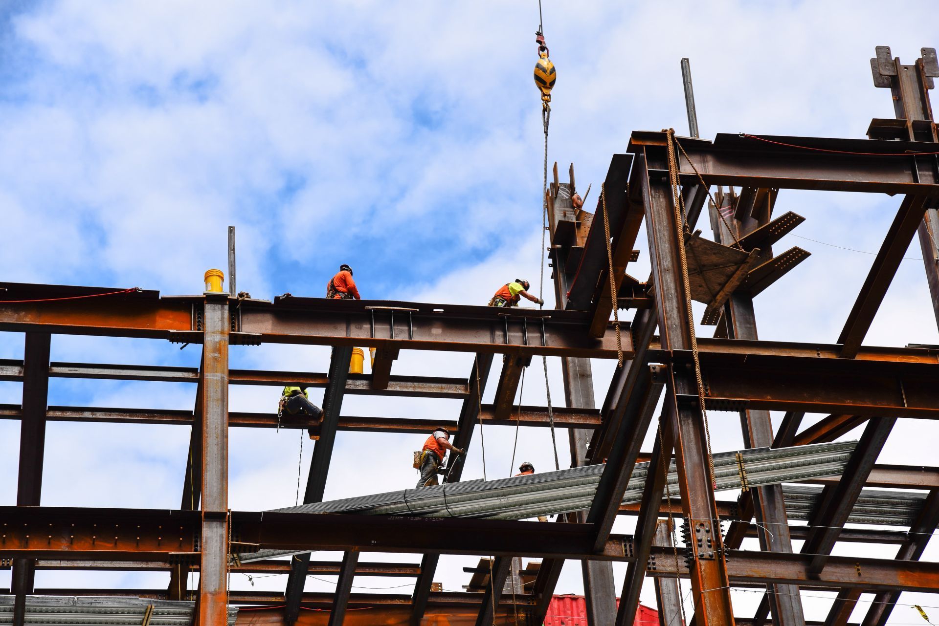 Construction workers on a steel frame with a crane hoisting materials against a blue sky