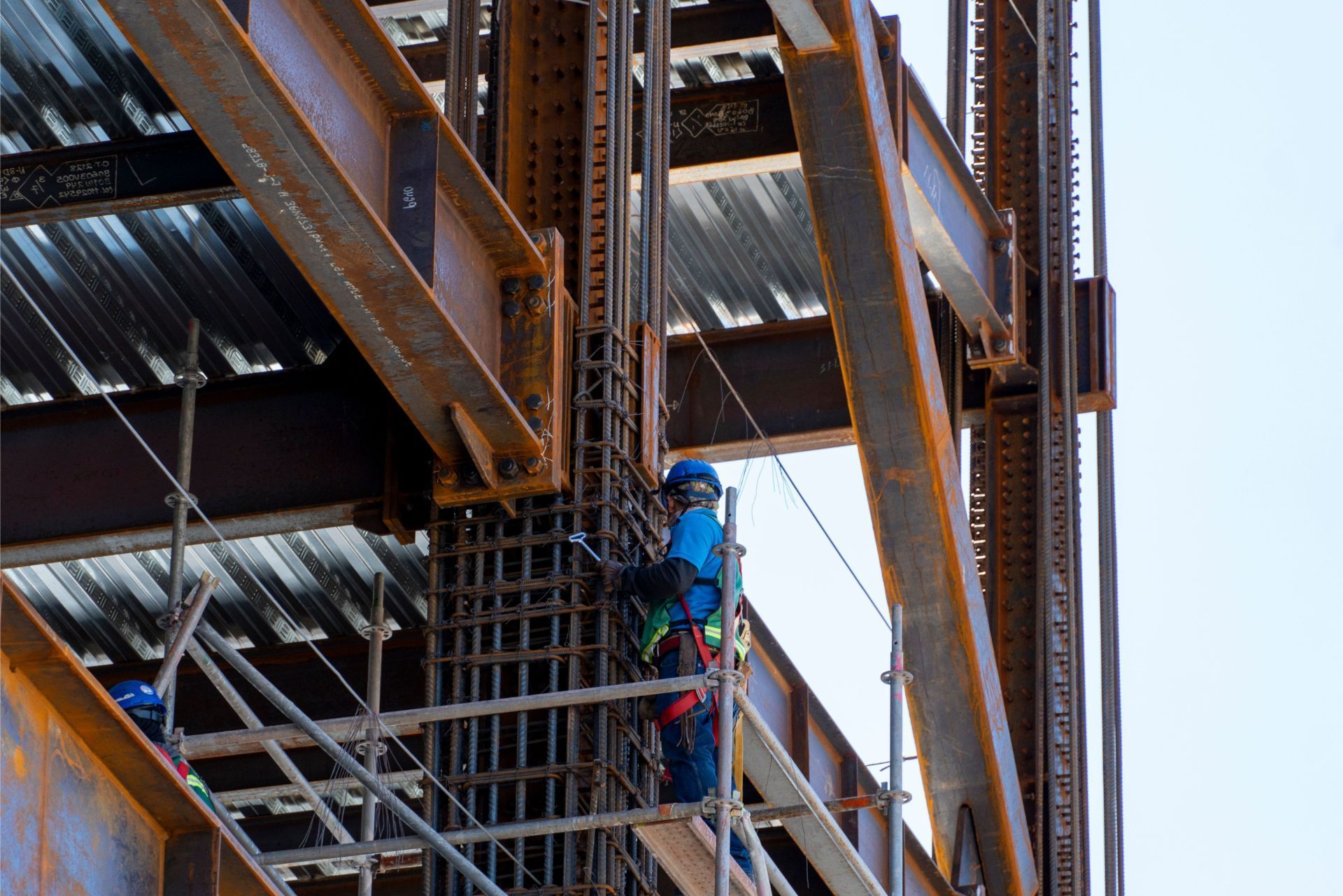 Construction worker in blue harness on steel scaffolding beside a building frame