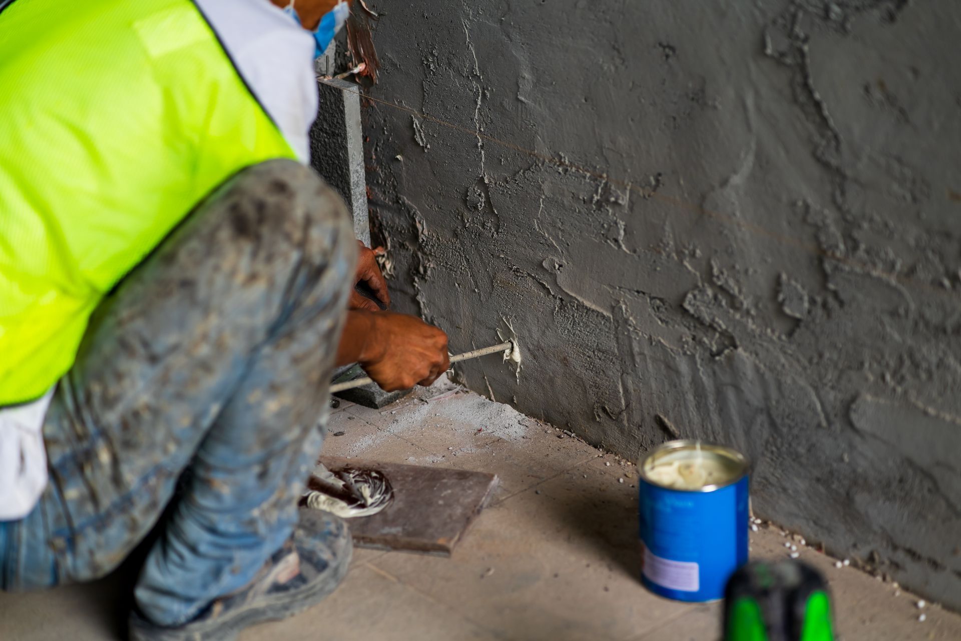 Worker applying plaster to a wall beside a blue paint can and trowel on the floor