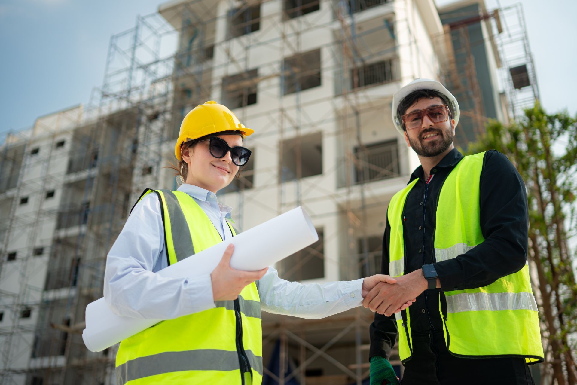 Two construction workers in yellow safety vests and hard hats reviewing plans at a building site