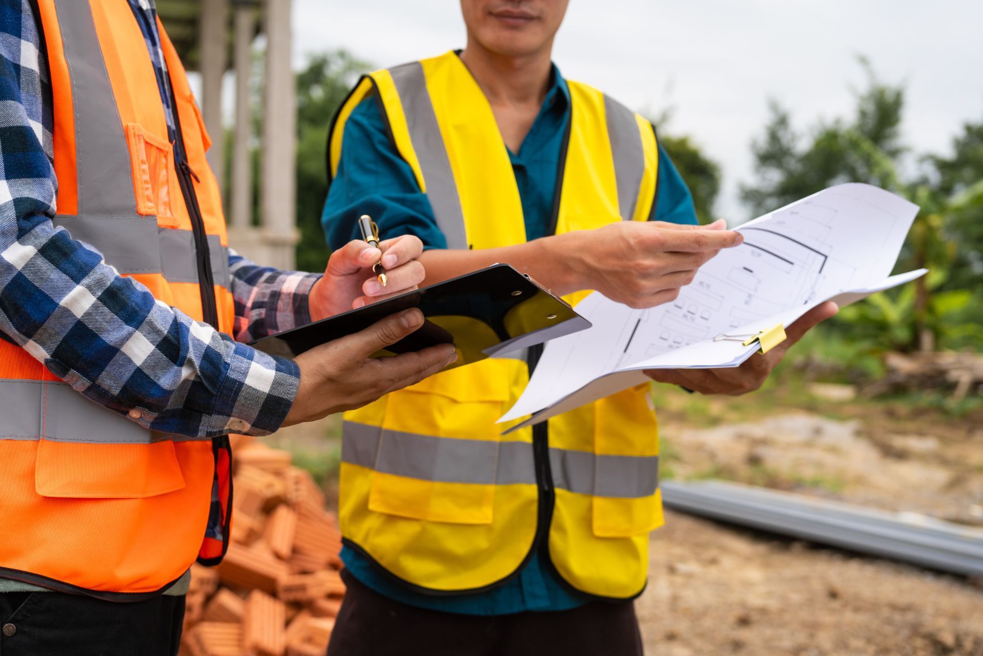 Two construction workers in safety vests reviewing blueprints at a building site