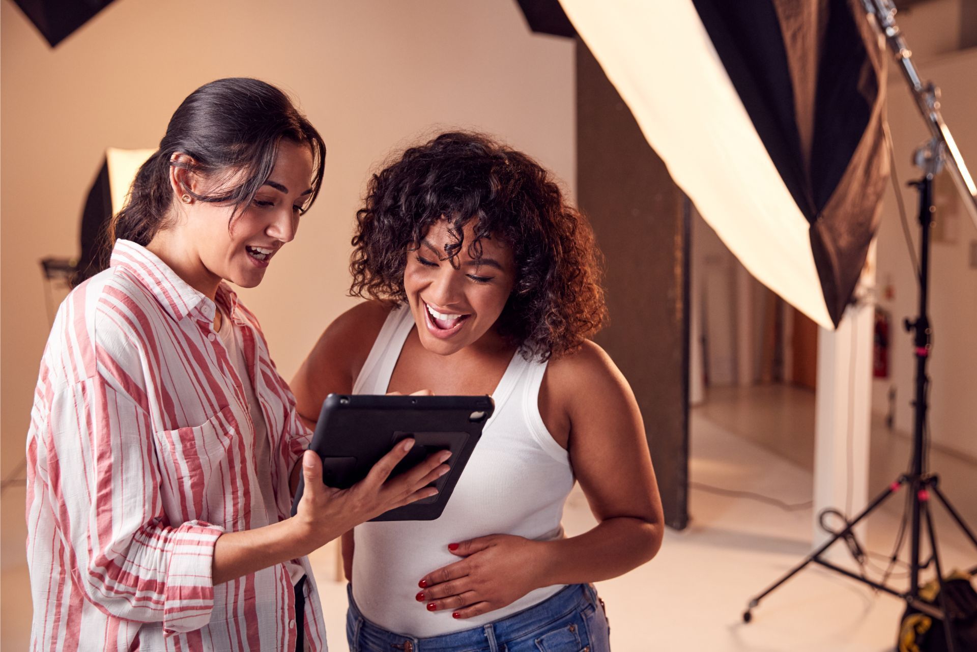Two people smiling at a tablet in a photo studio with lighting equipment