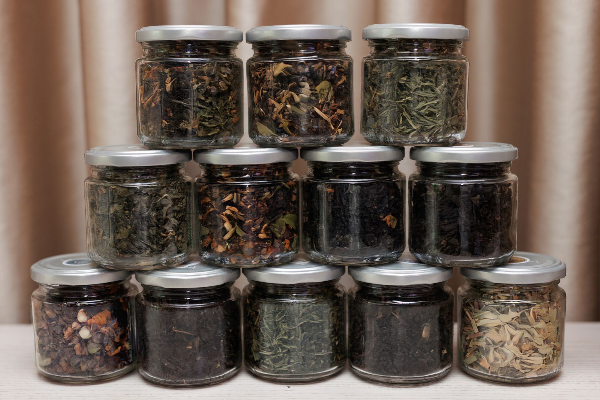 Stacked clear jars filled with loose tea leaves on a table against beige curtains