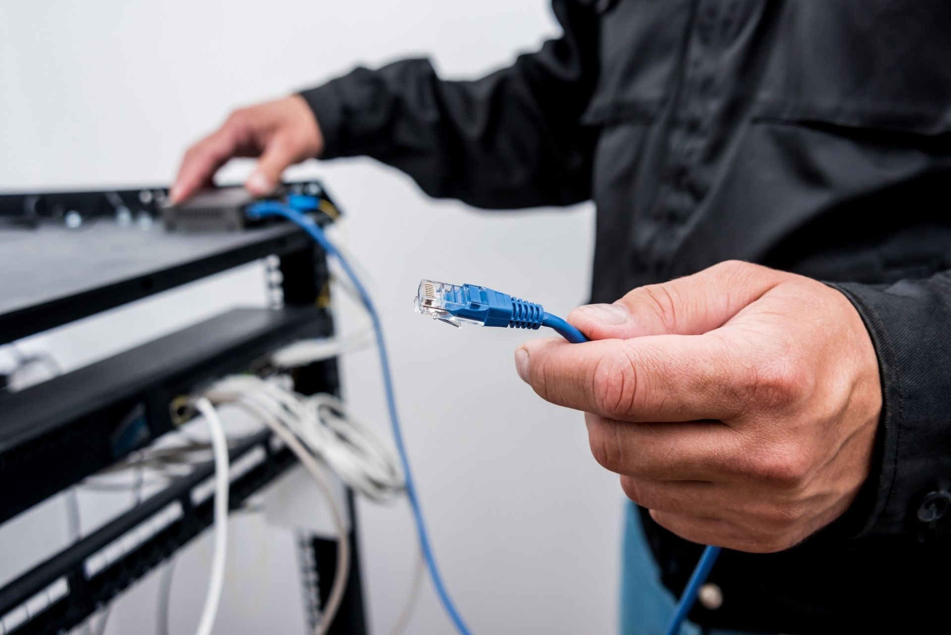 A person in a black shirt holds a blue Ethernet cable while working at a server rack.