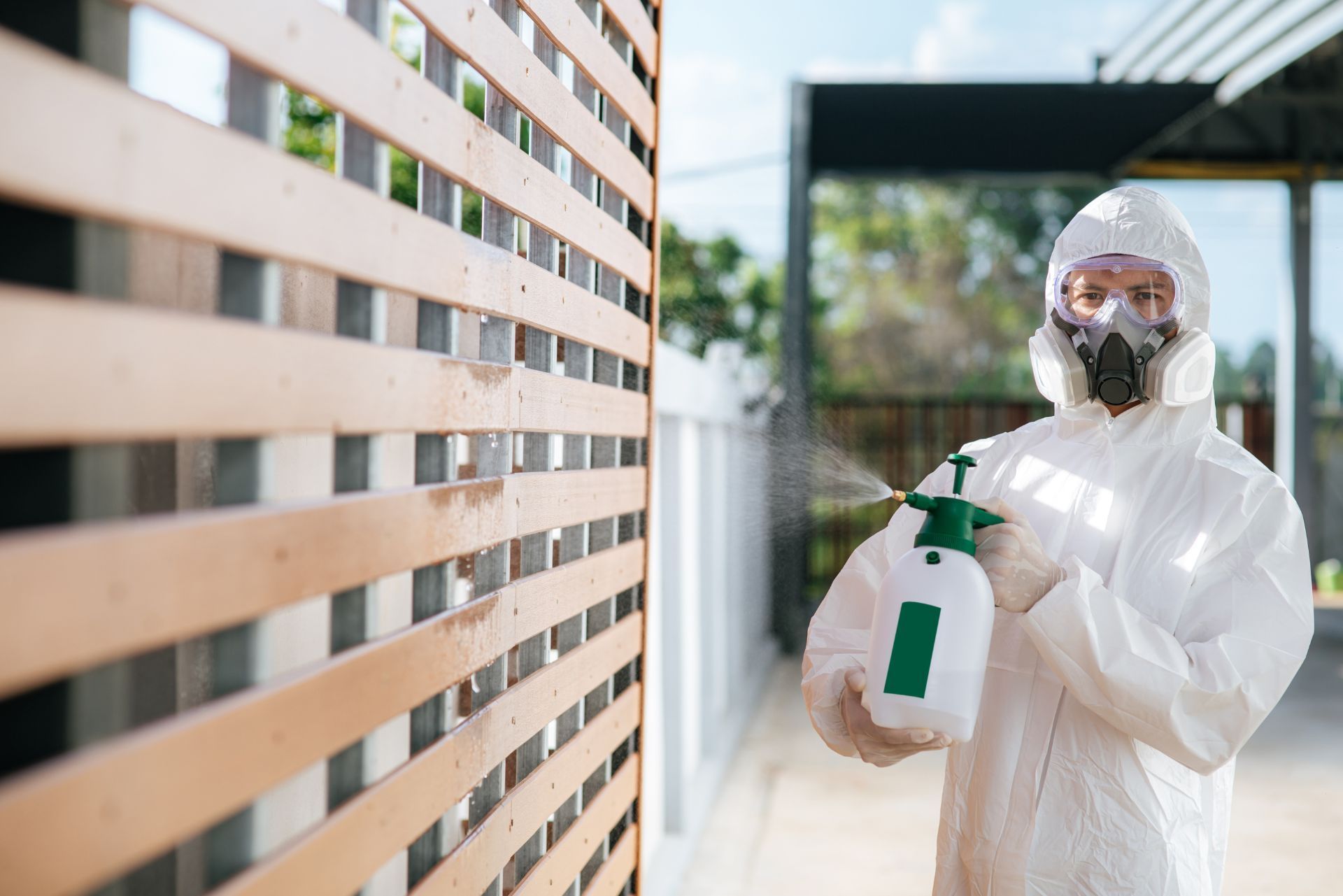 Person in protective suit disinfecting a fence with a spray bottle outdoors