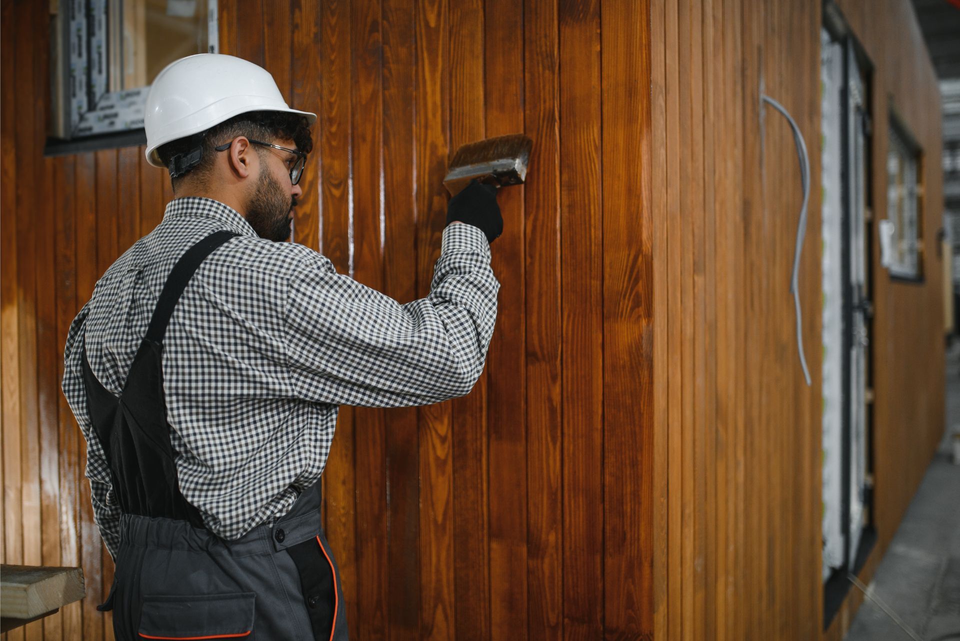 Worker in a hard hat paints a wooden wall indoors.